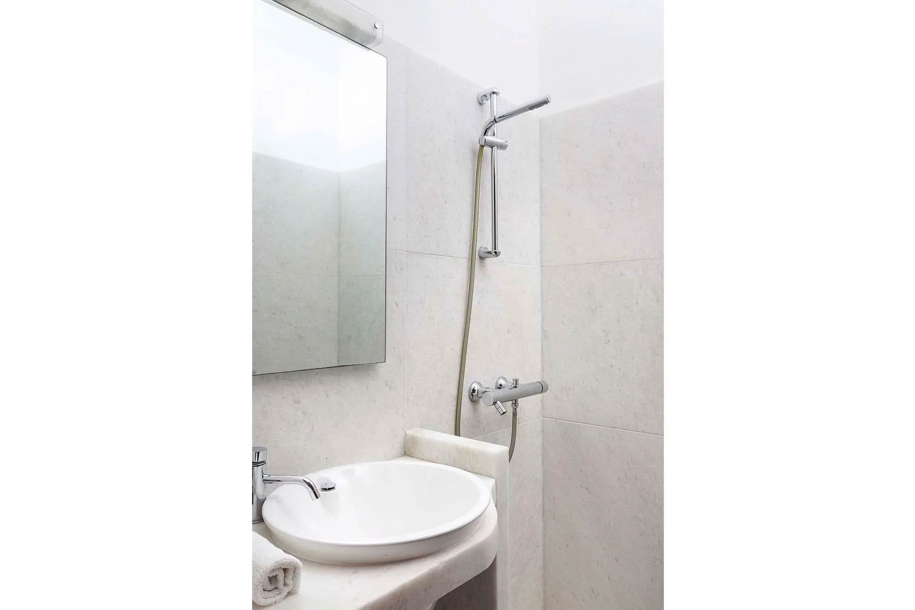 A bright bathroom with a sink, mirror, and wall-mounted shower.