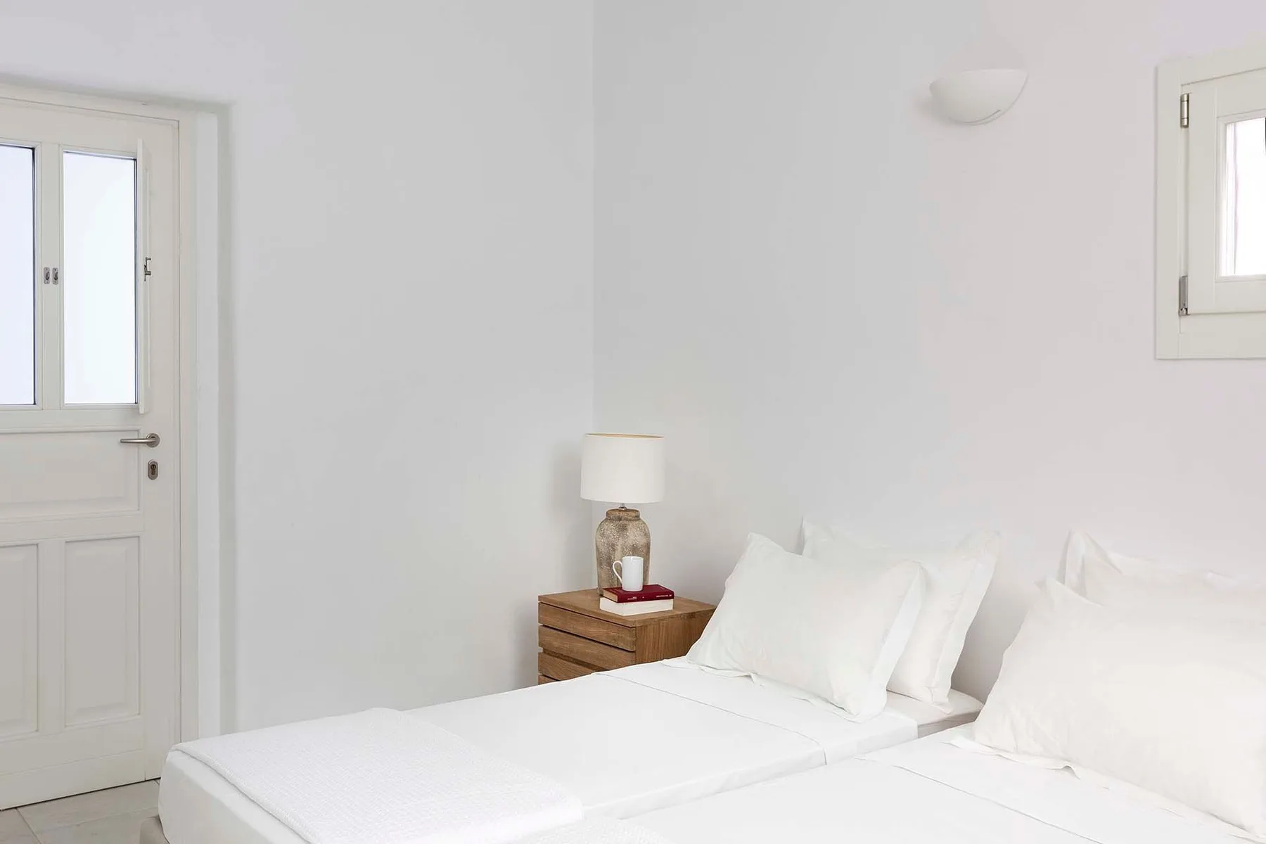 A bright bedroom with white bedding and a wooden bedside table.