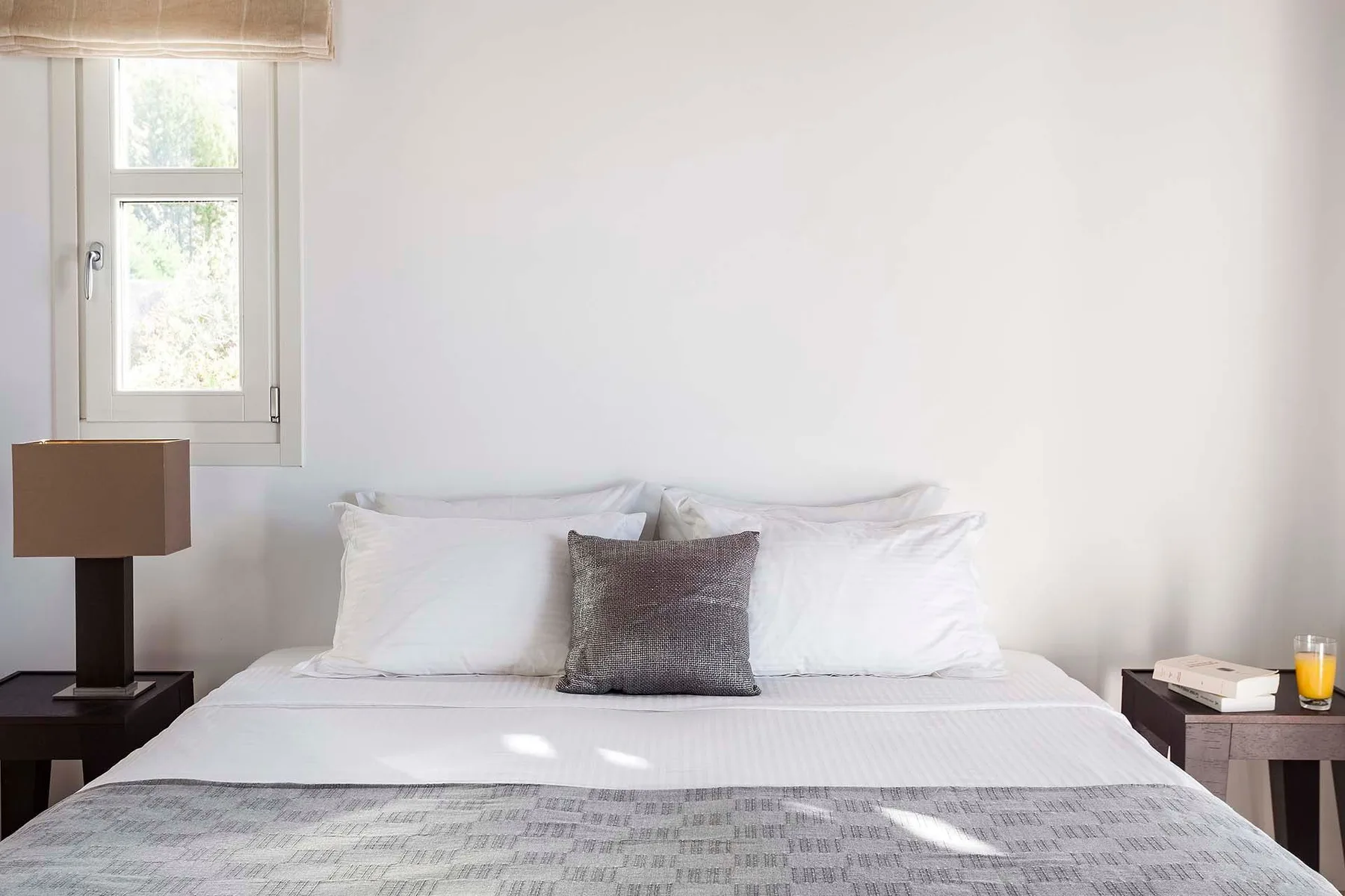 A bedroom with a neatly made bed and a window beside it.