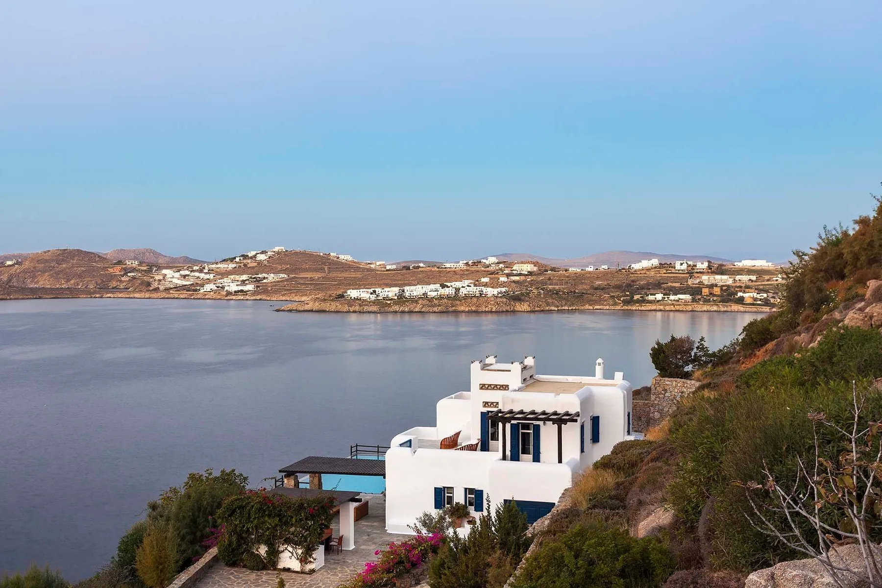 A white building sits beside a calm bay, with hills across the water.