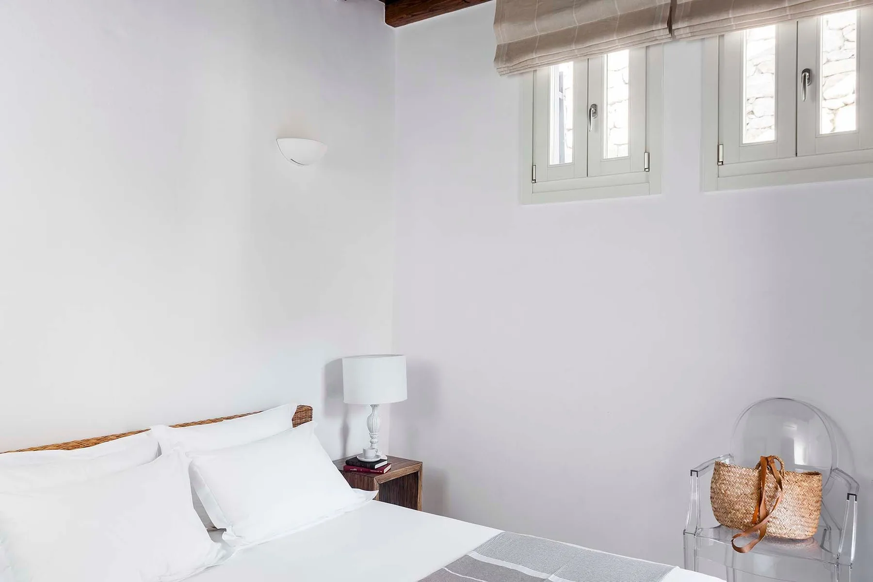 A bright bedroom with white bedding and high windows.