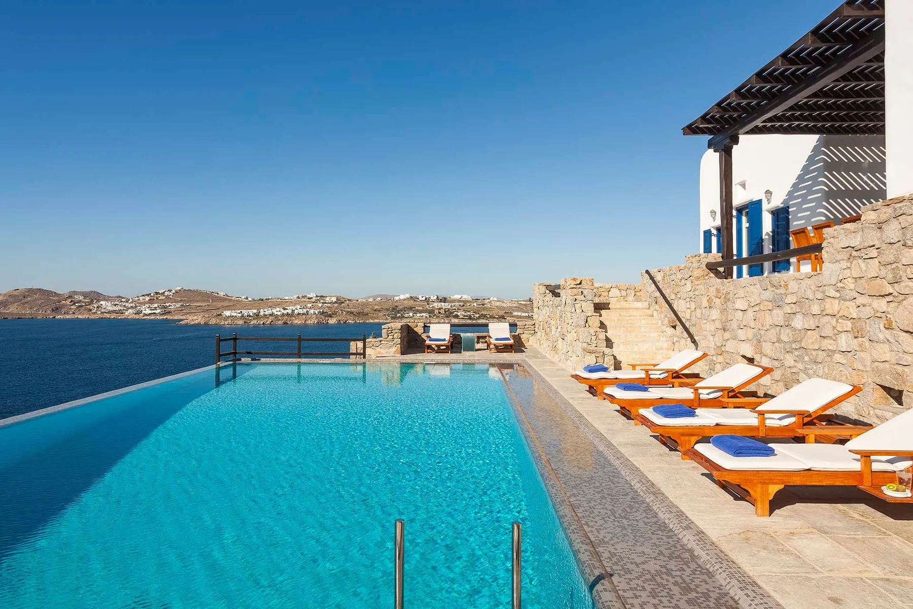 An outdoor swimming pool beside a stone terrace with sun loungers.