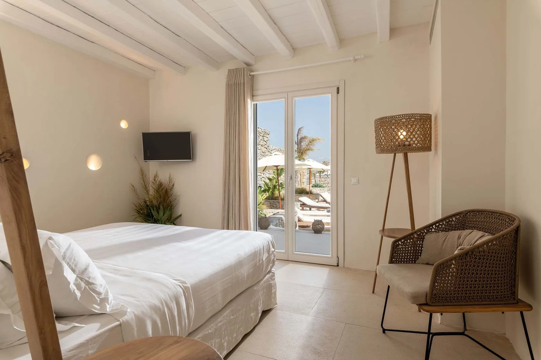A bright bedroom with a bed, glass doors, and woven seating.