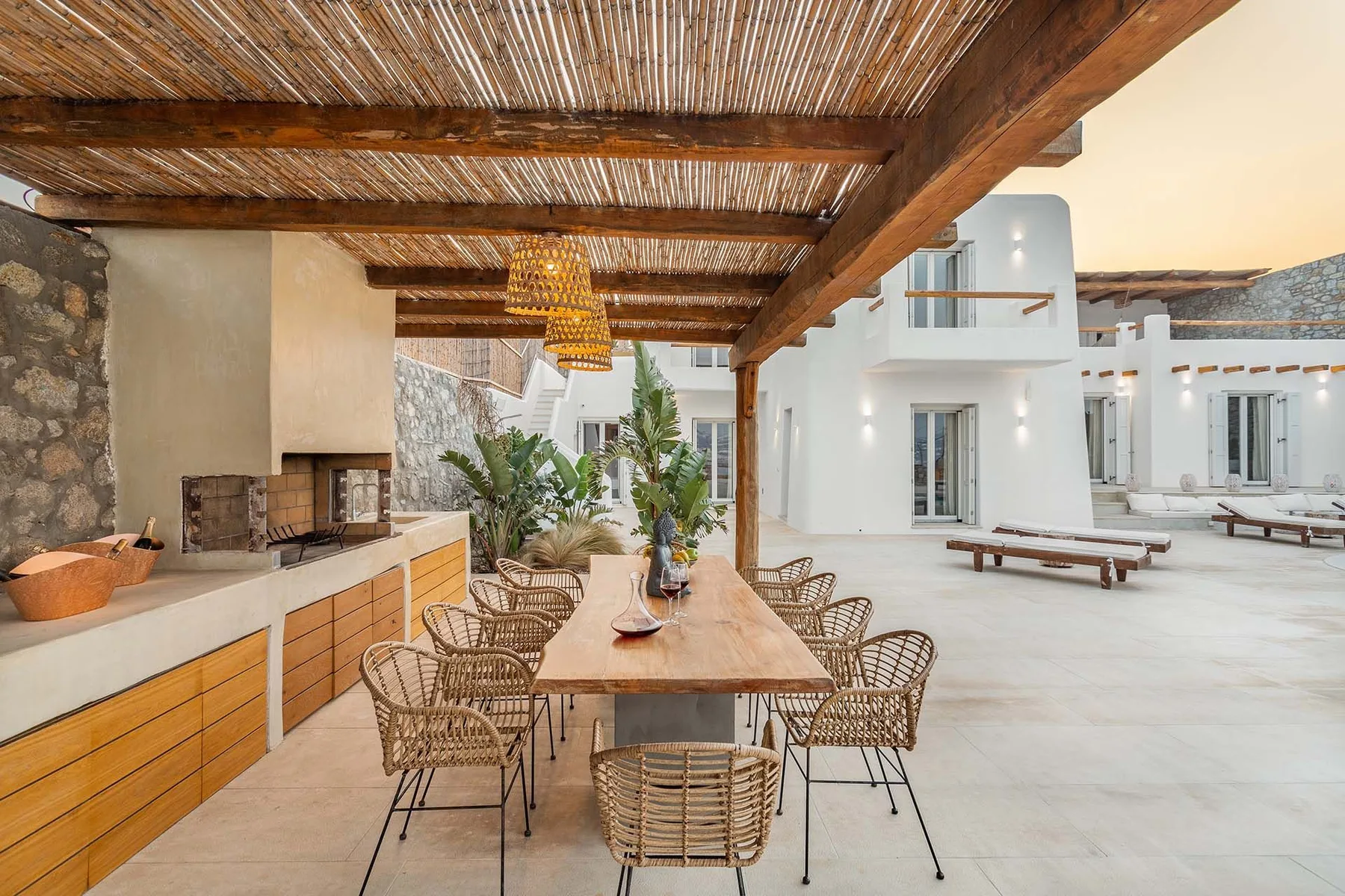 An outdoor dining area sits beneath a wooden pergola beside a white courtyard.