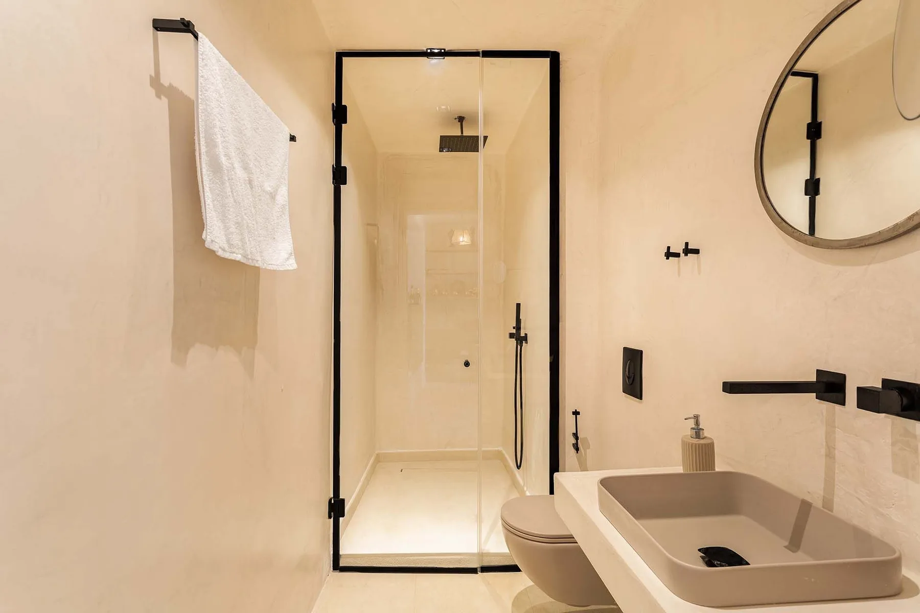 A bathroom with a glass shower and a sink beneath a round mirror.