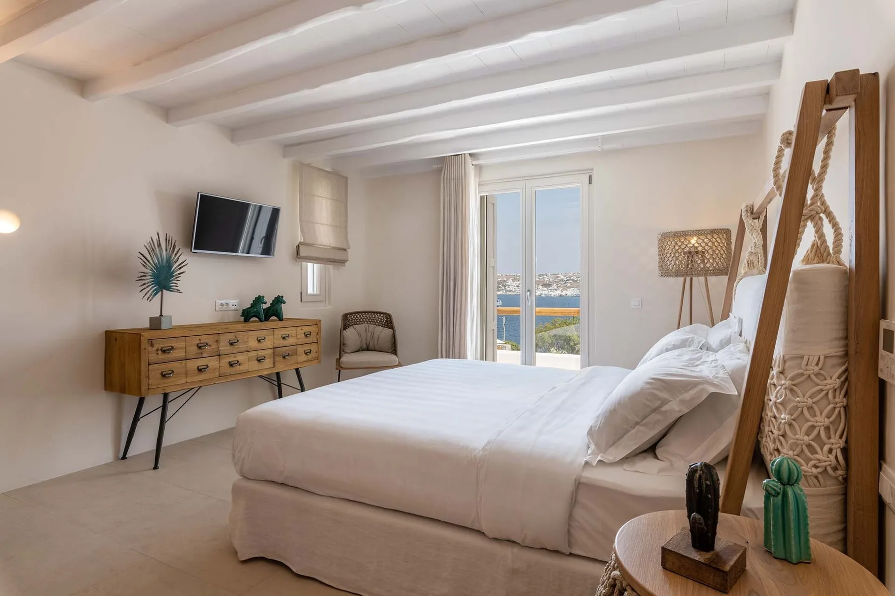 A bright bedroom with a neatly made bed and glass doors opening onto a balcony.
