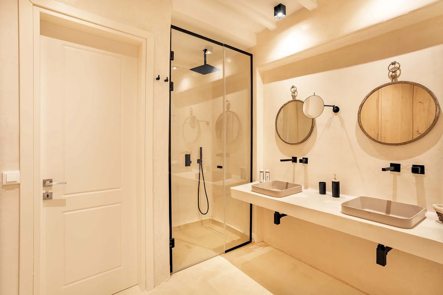A bright bathroom with a glass shower and a long vanity with two sinks.
