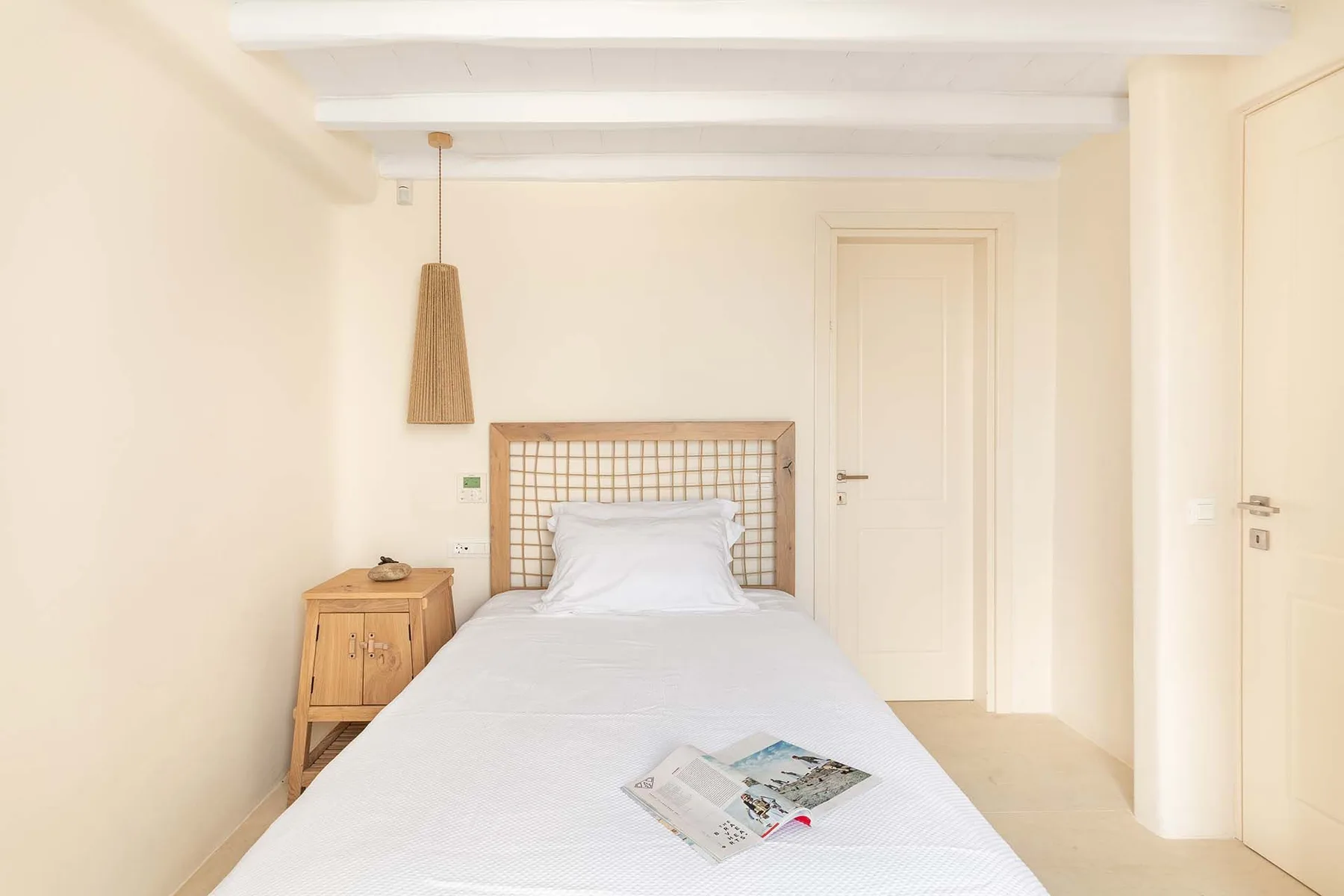 A bright bedroom with a single bed, a wooden headboard, and a bedside table.