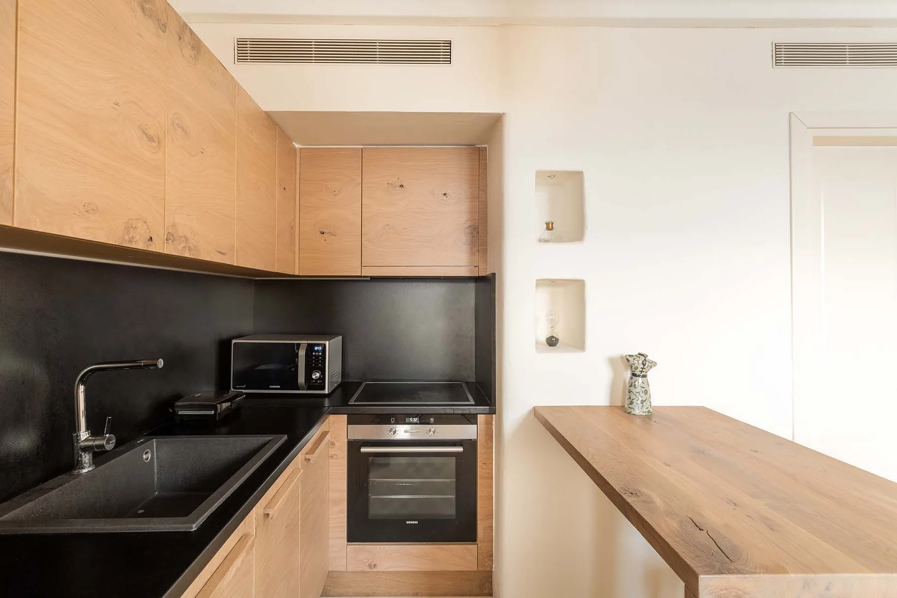 A compact kitchen with wood cabinetry, dark countertops, and a built-in oven.