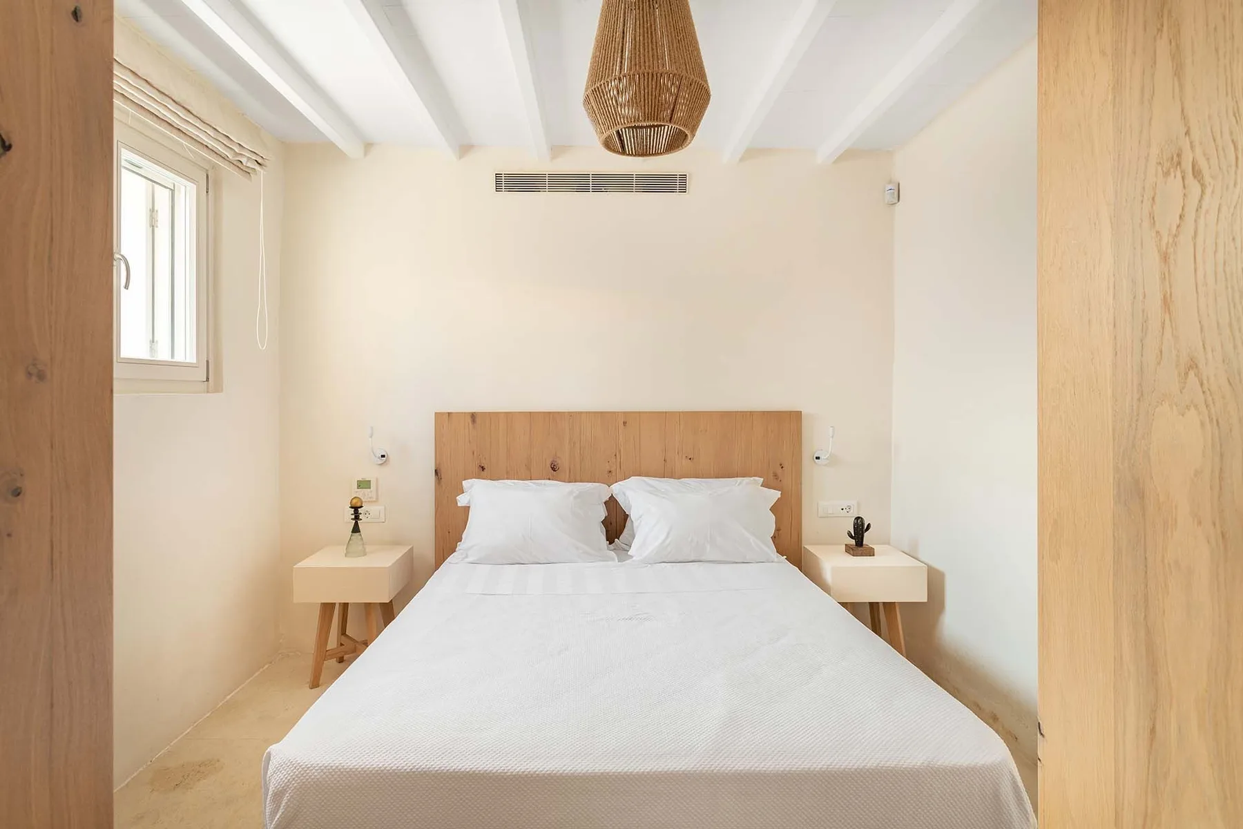A bright bedroom with a neatly made bed and wooden headboard.