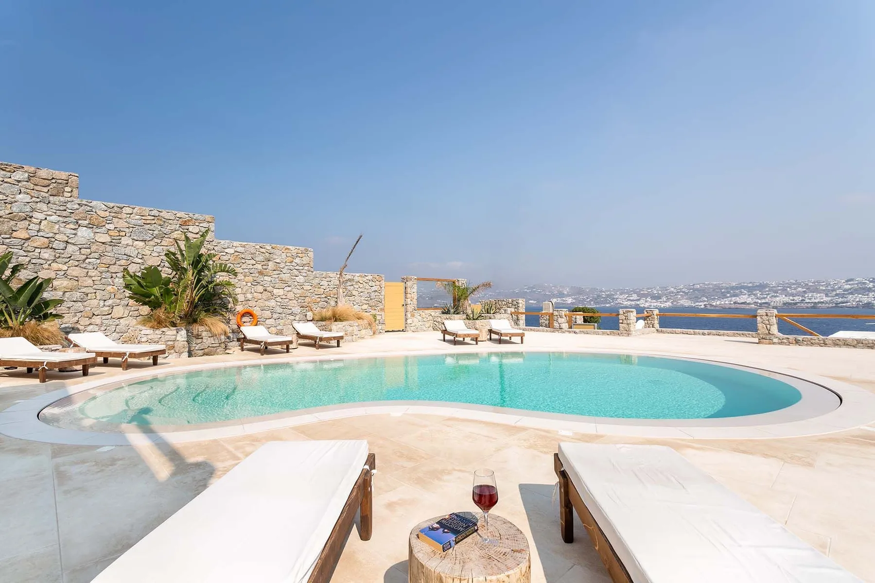 An outdoor swimming pool is surrounded by loungers and stone walls.
