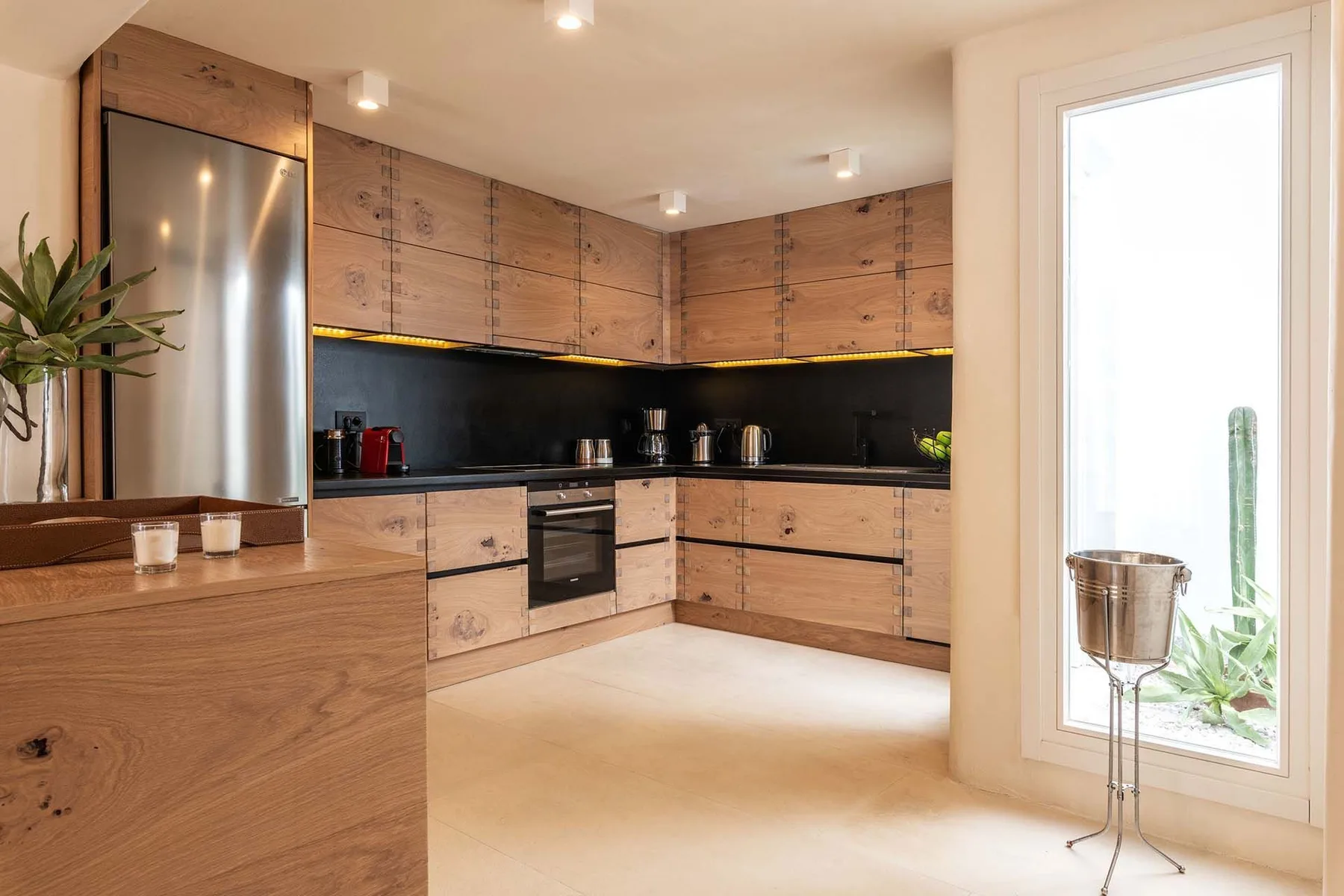 A modern kitchen with wood cabinetry, a dark backsplash, and a large window.