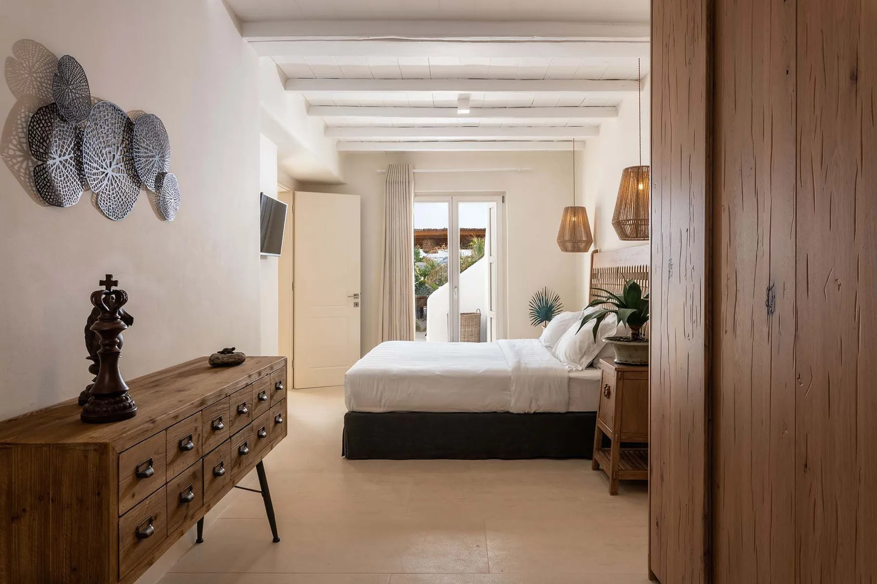 A bedroom with a bed, wooden dresser, and glass doors opening to a patio.
