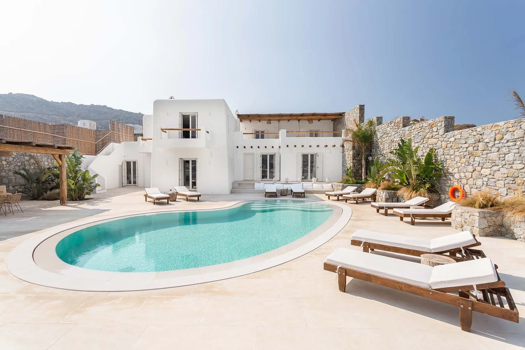 A curved swimming pool and sun loungers sit in the courtyard of a white building.