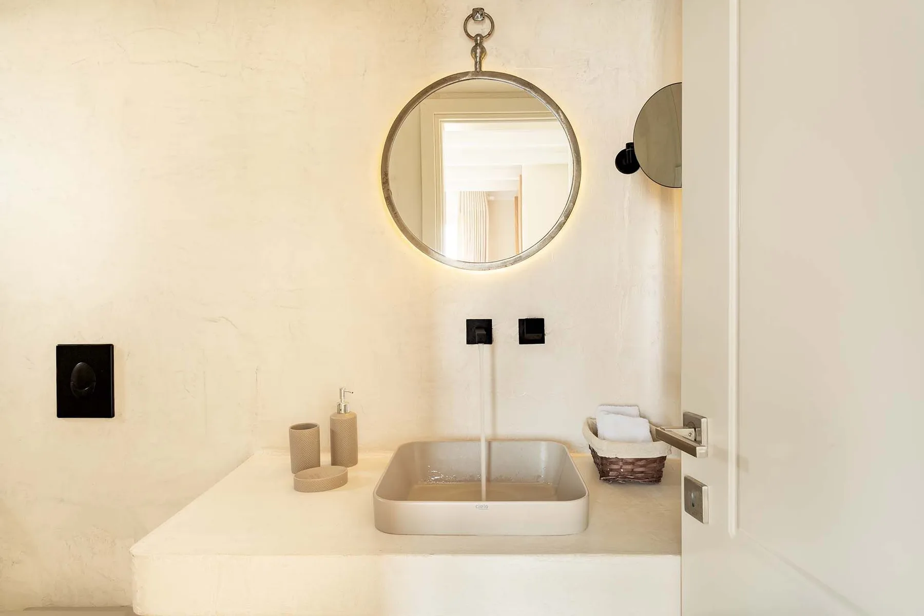 A bathroom vanity with a vessel sink, round mirror, and wall-mounted faucet.