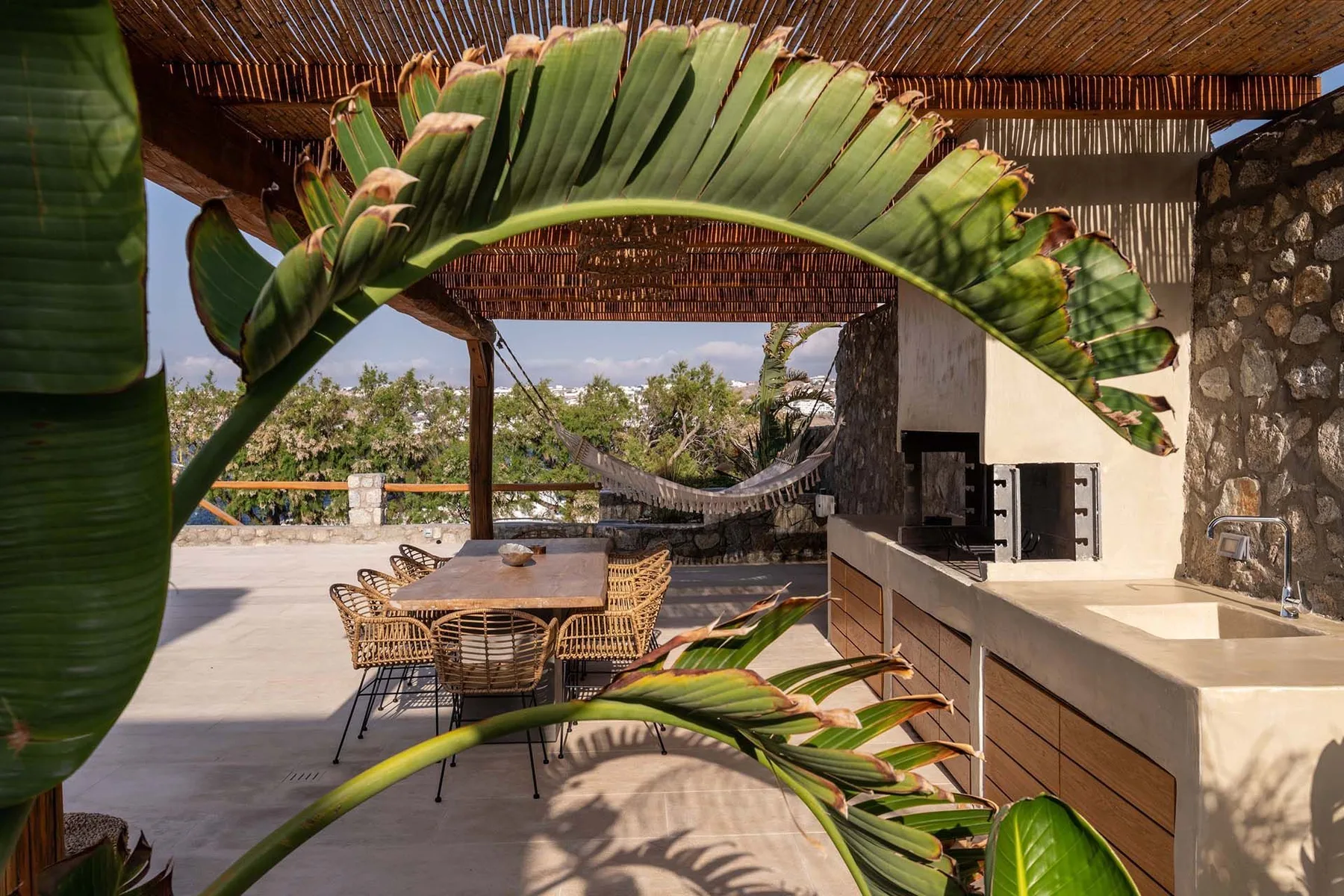 An outdoor dining area with a counter and hammock beneath a shaded roof.