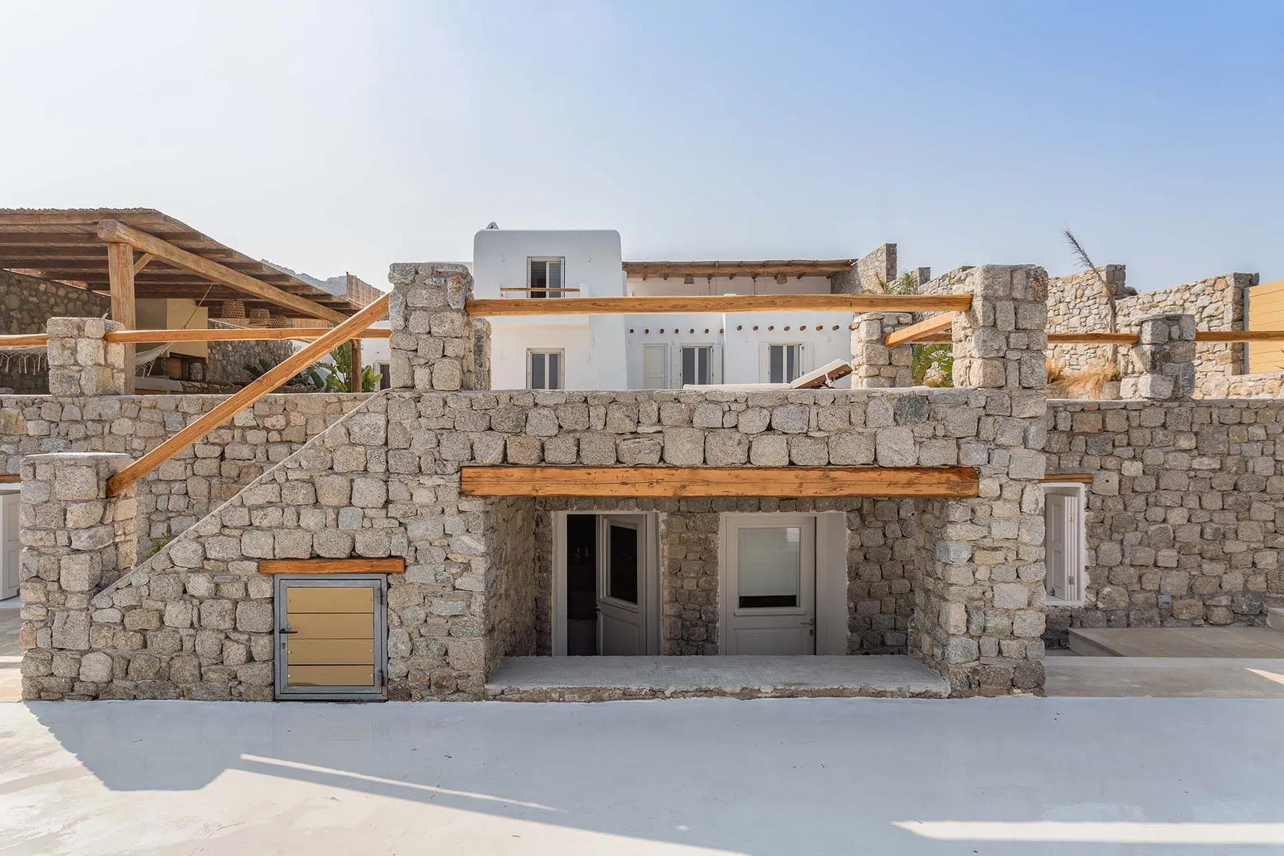 A stone building with a shaded entrance and a pale paved courtyard.