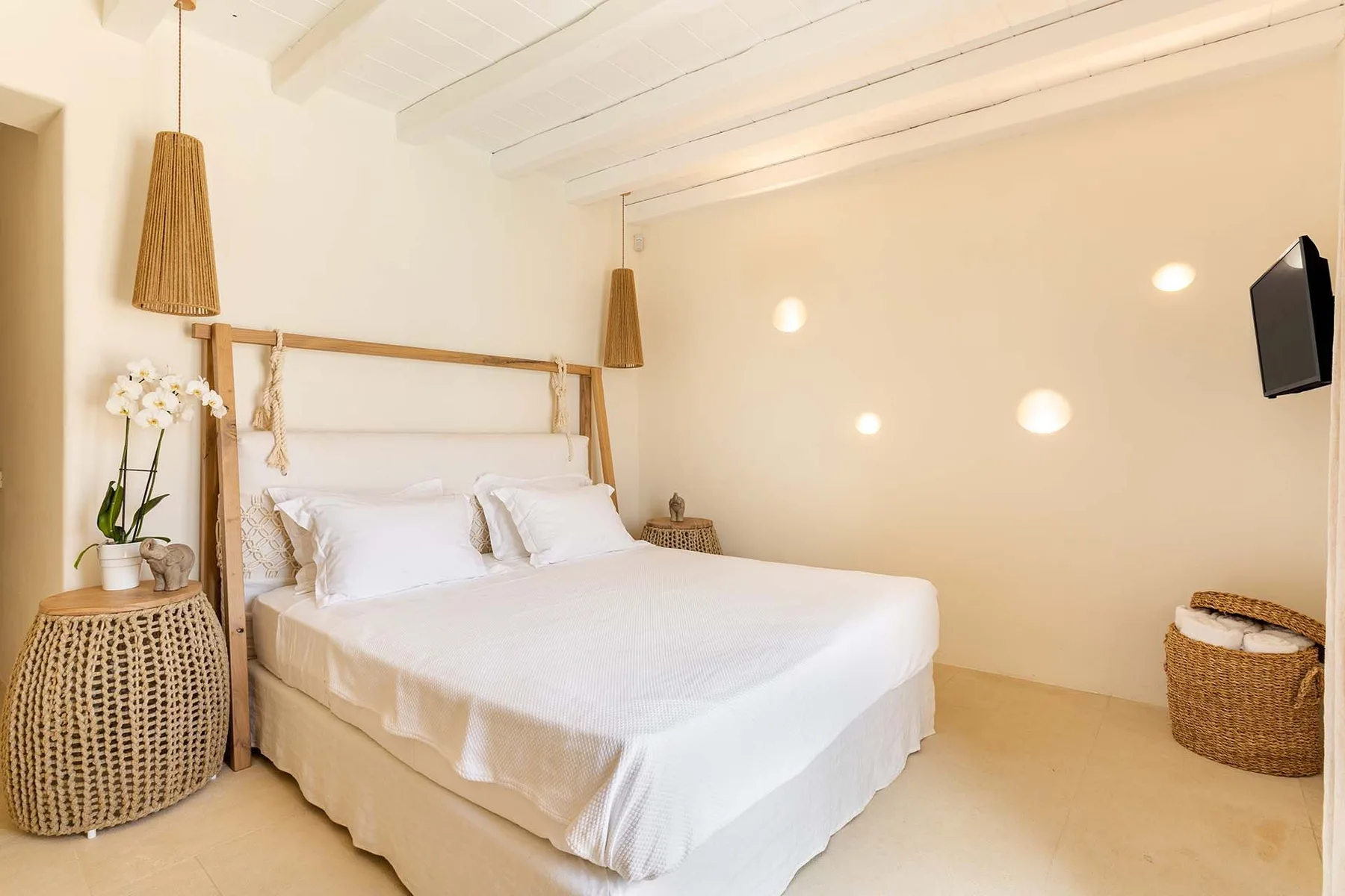 A bright bedroom with a neatly made bed and a wall-mounted television.