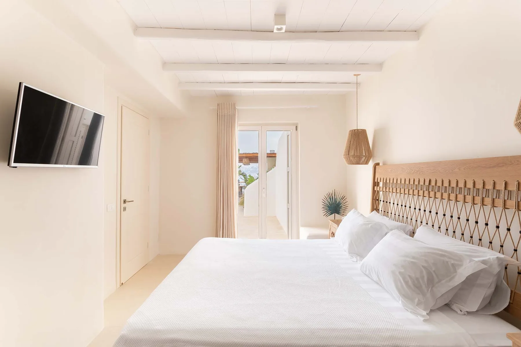 A bright bedroom with a bed, wall-mounted television, and a window.