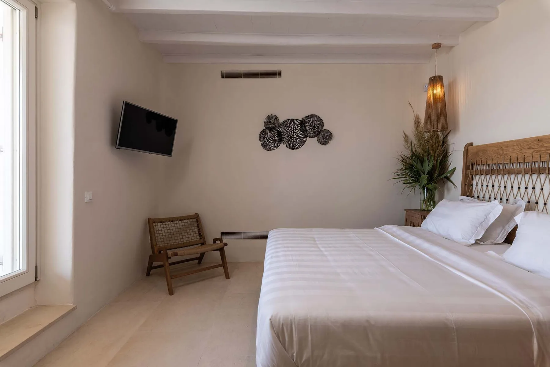 A bright bedroom with a bed, woven headboard, and wall-mounted television.
