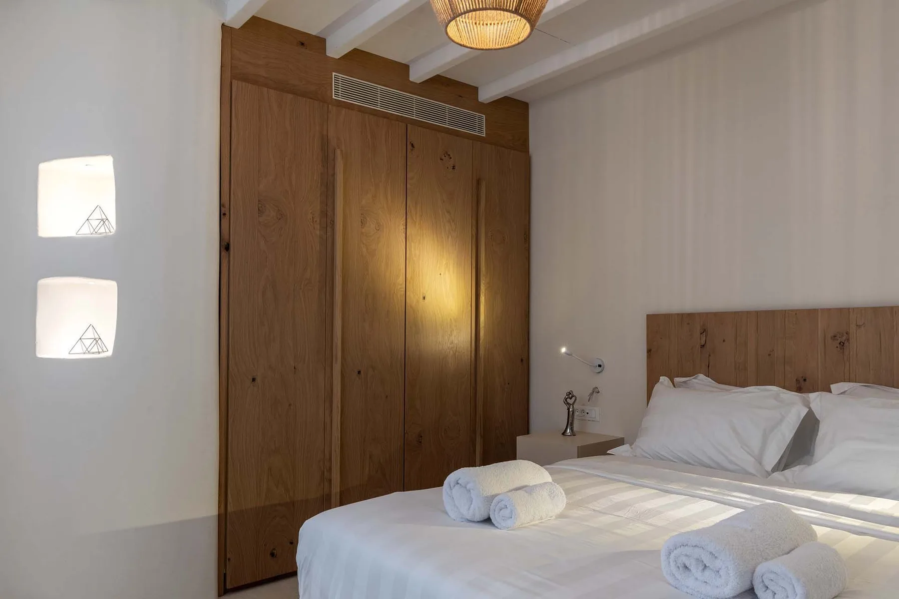 A bedroom with a wooden wardrobe and a bed topped with folded towels.