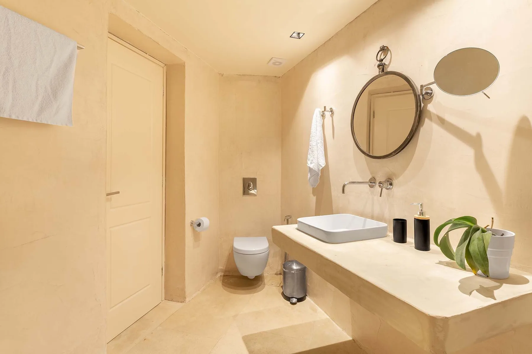 A bright bathroom with a sink, wall mirror, toilet, and light-colored surfaces.