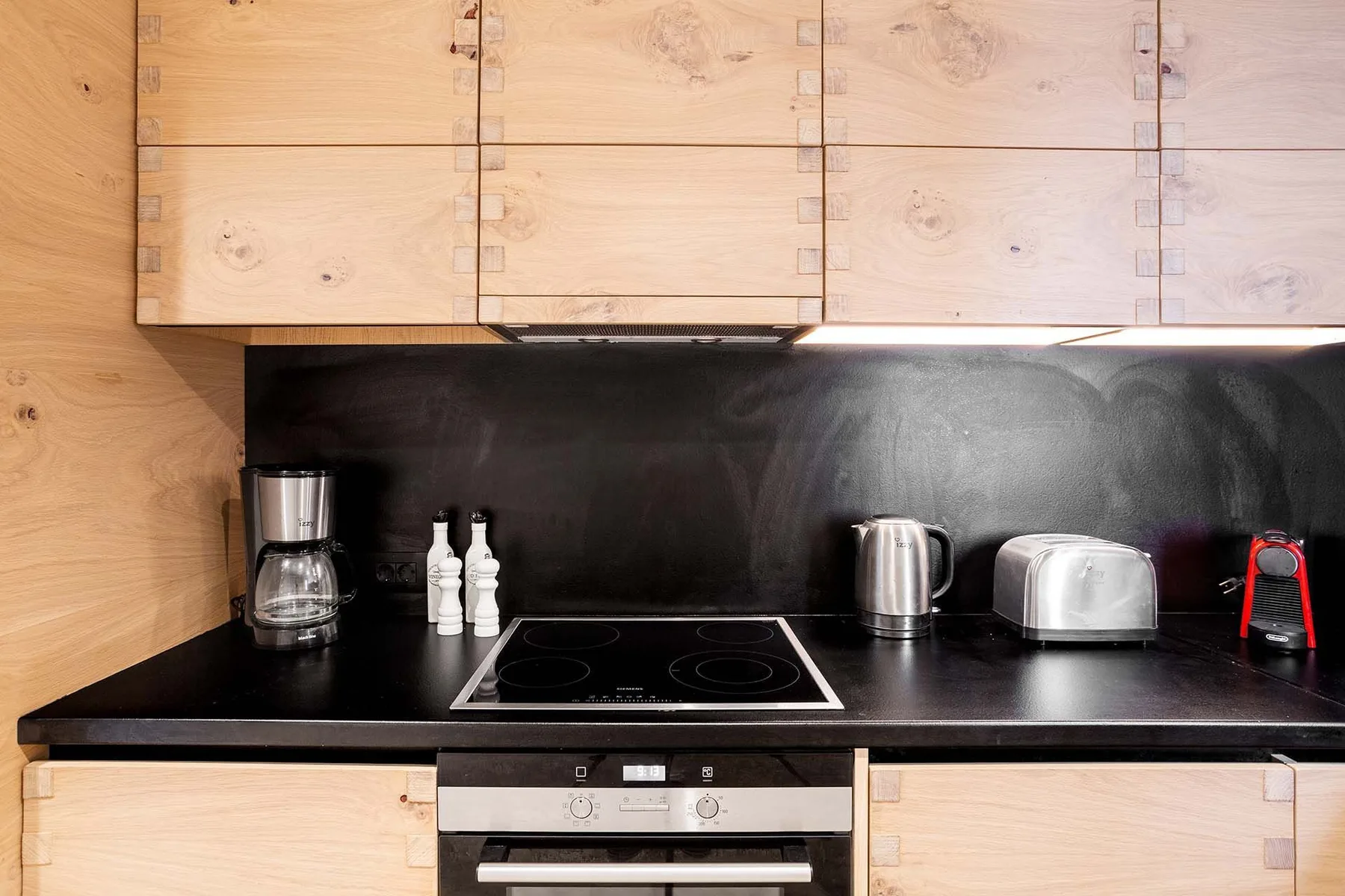 A modern kitchen with a black countertop, cooktop, and light wood cabinets.