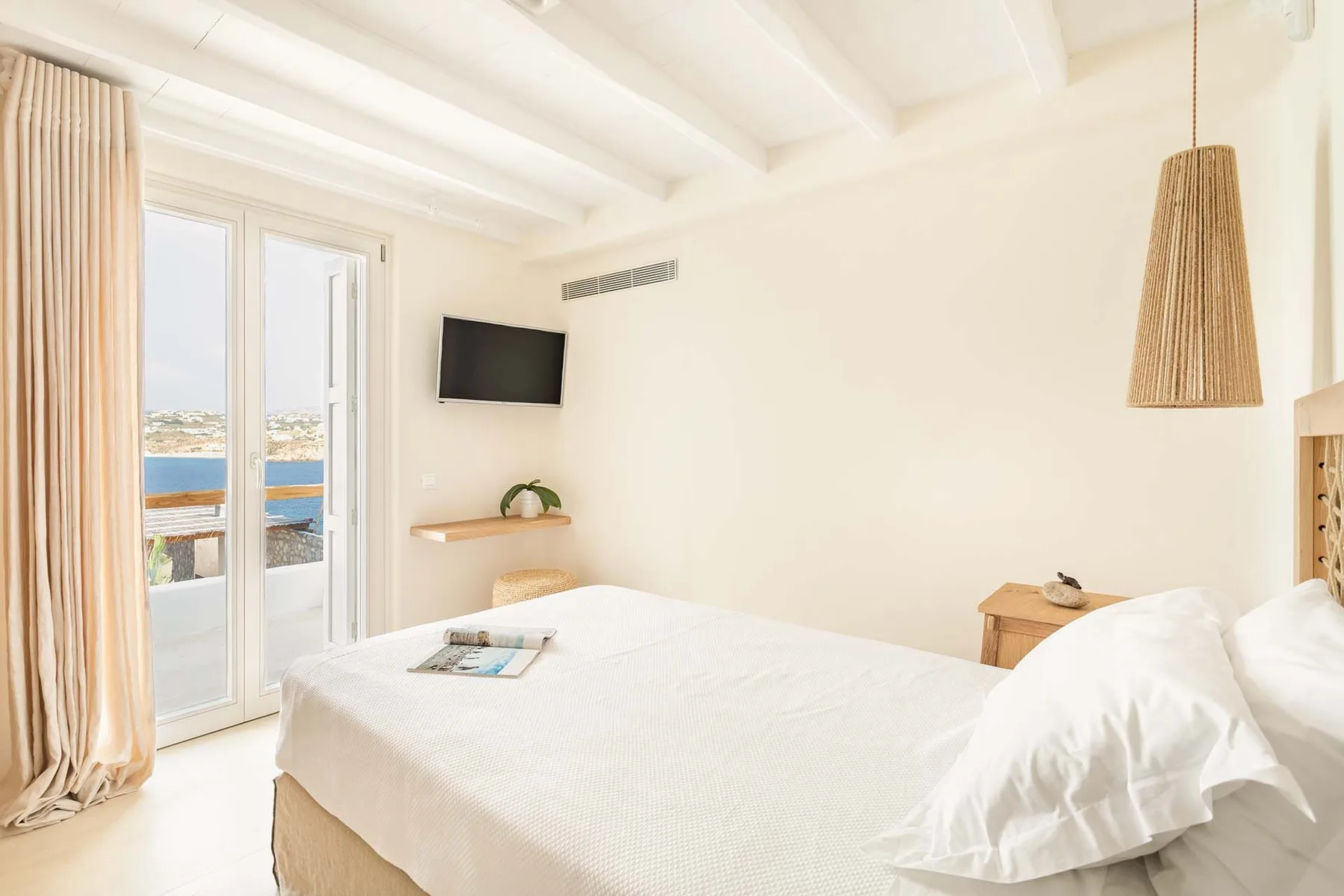 A bright bedroom with a bed beside glass doors opening onto a balcony.