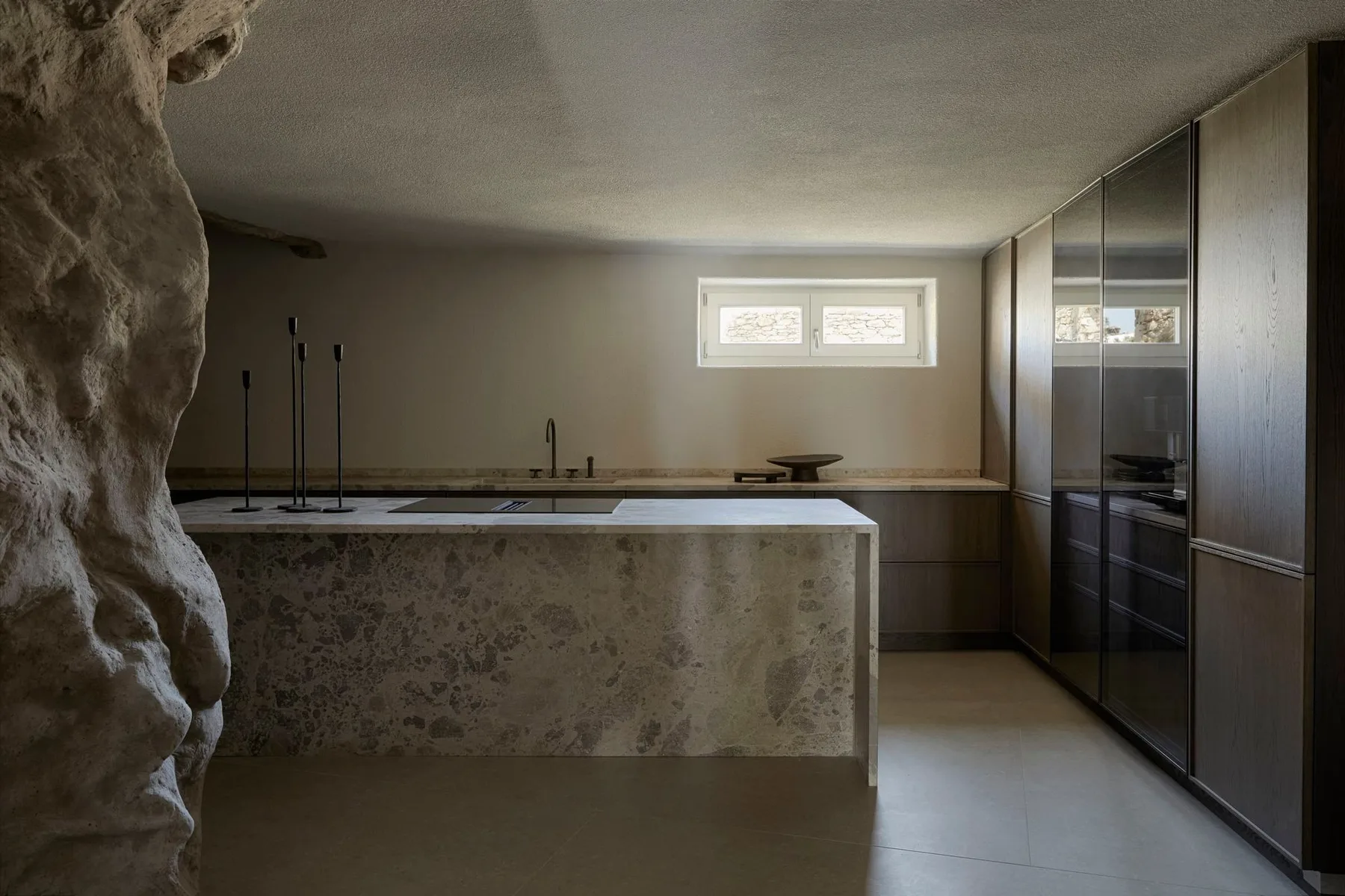 A modern kitchen with a stone island and dark cabinets.