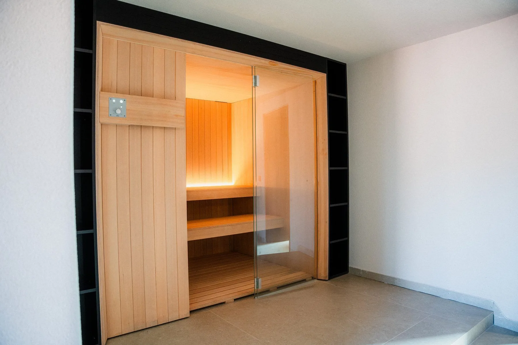 A sauna room with a wooden bench and glass door.