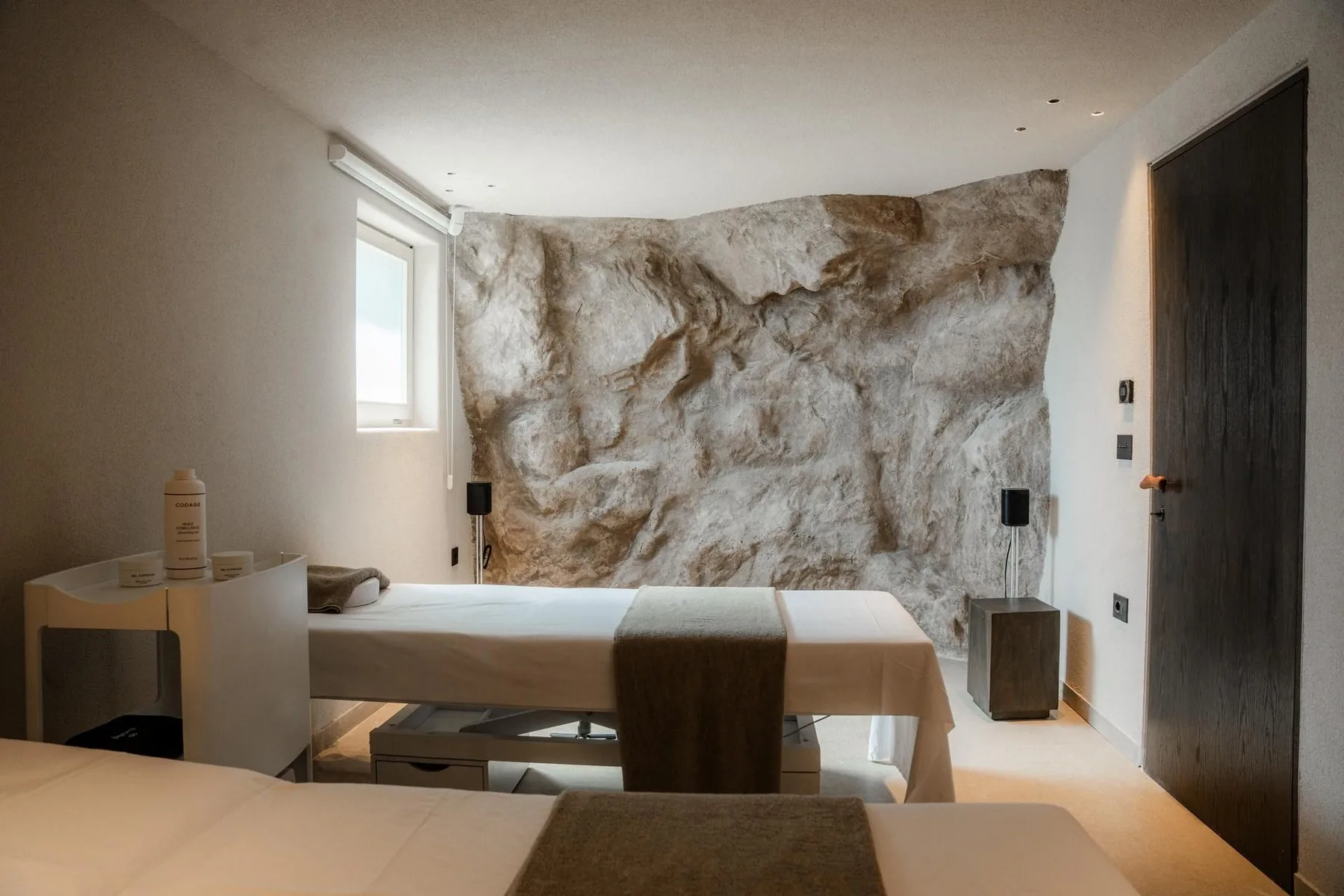 A bedroom with a bed, a window, and a textured stone wall.