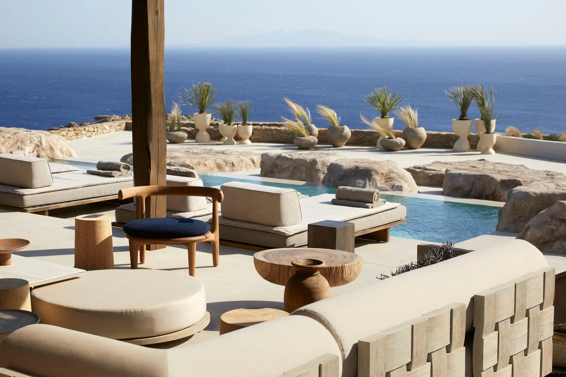 A seaside pool terrace with cushioned seating and potted plants overlooking the ocean.