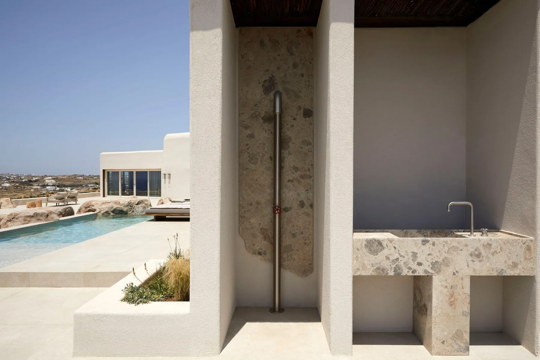 An outdoor shower area beside a pool, with a stone shower wall and built-in basin.