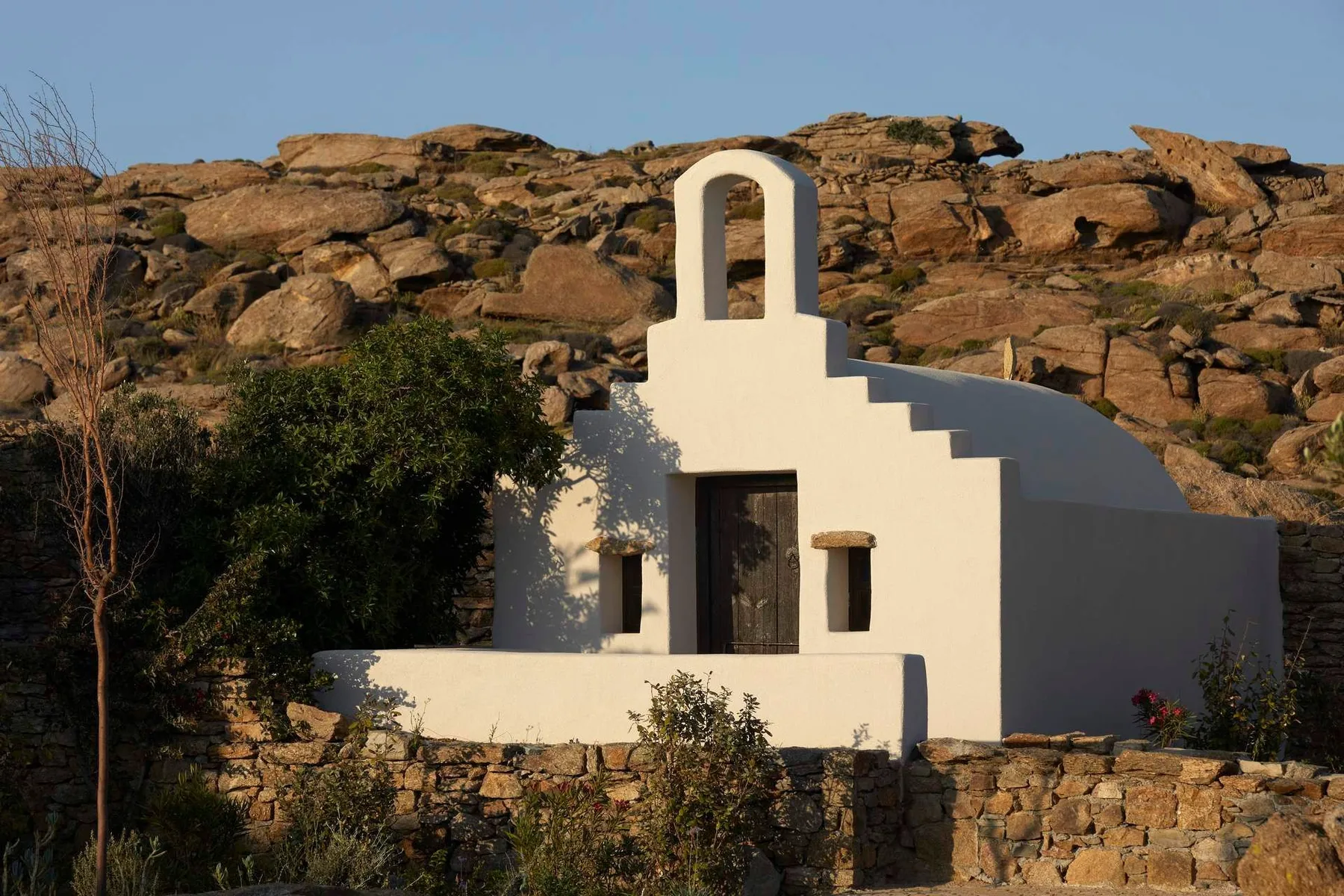 A small white building with a stepped roof stands among rocky hills.
