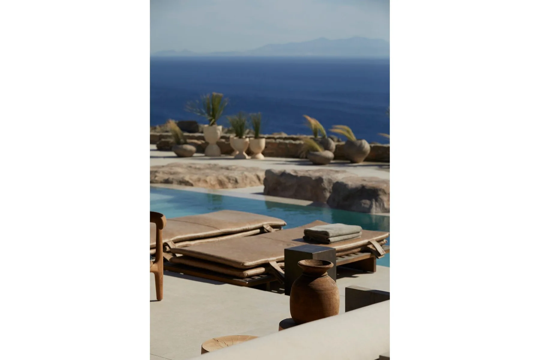 A poolside terrace overlooks the sea, with loungers and potted plants.