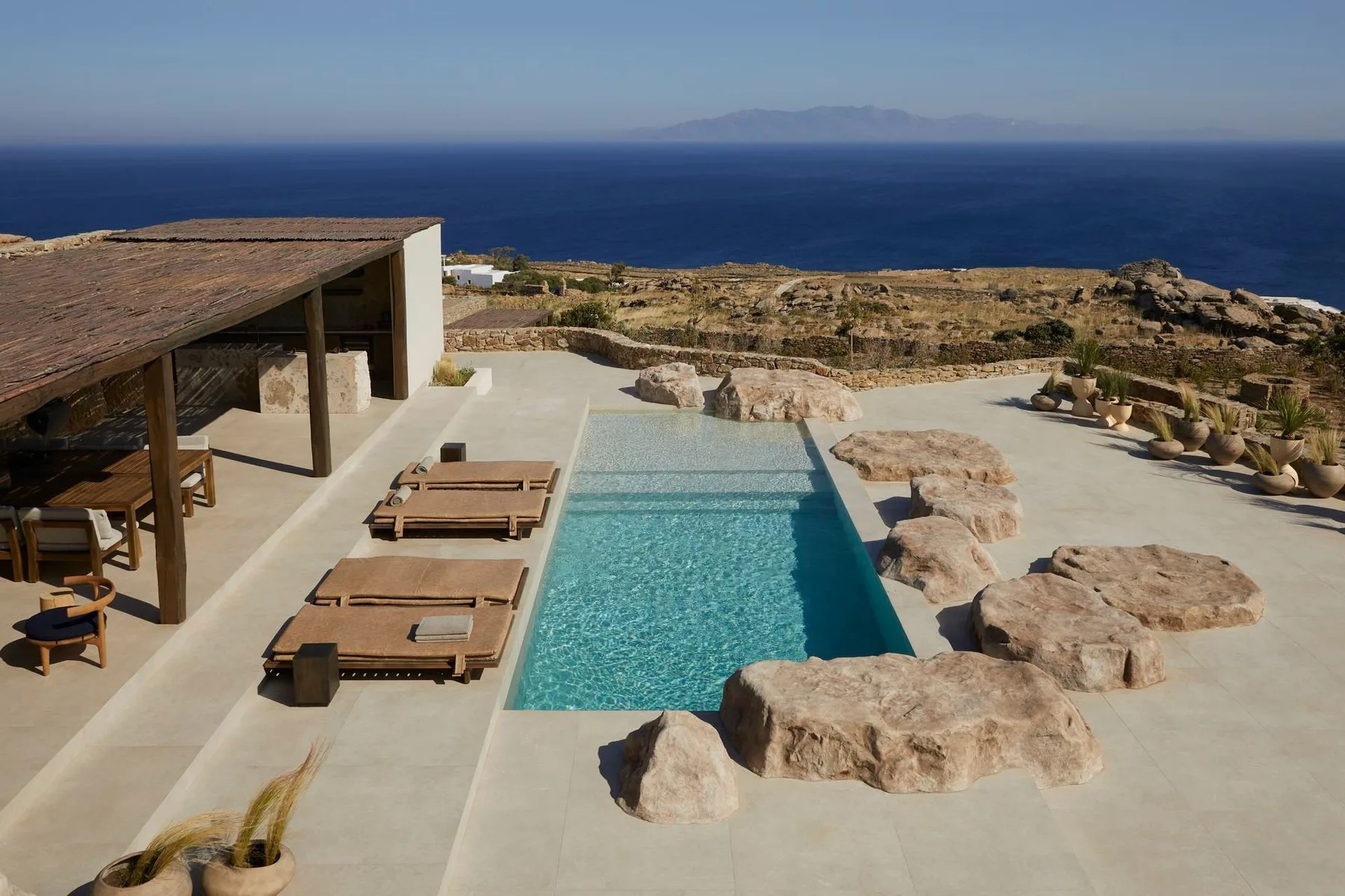 A swimming pool and sun loungers overlook the sea from a rocky terrace.