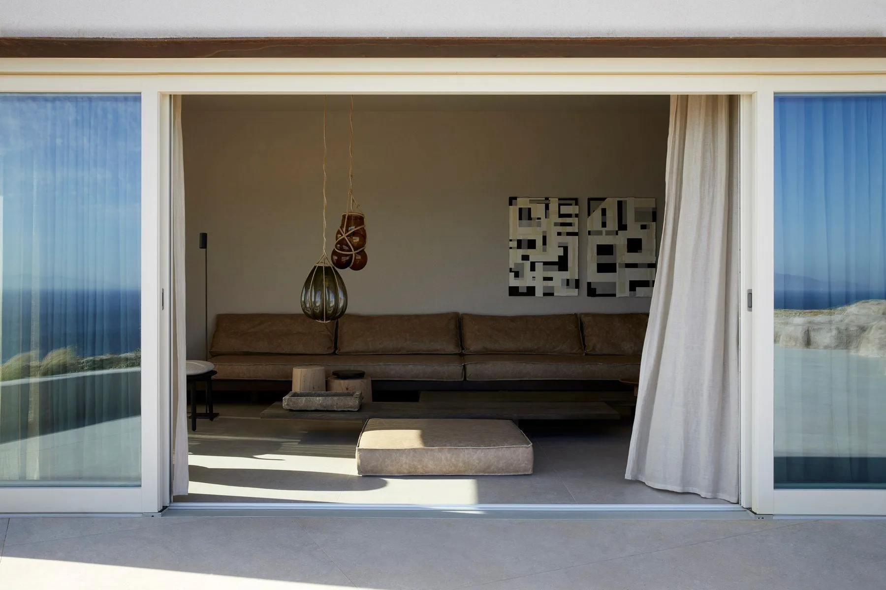 A living room opens onto a balcony, with a long sofa and hanging light.