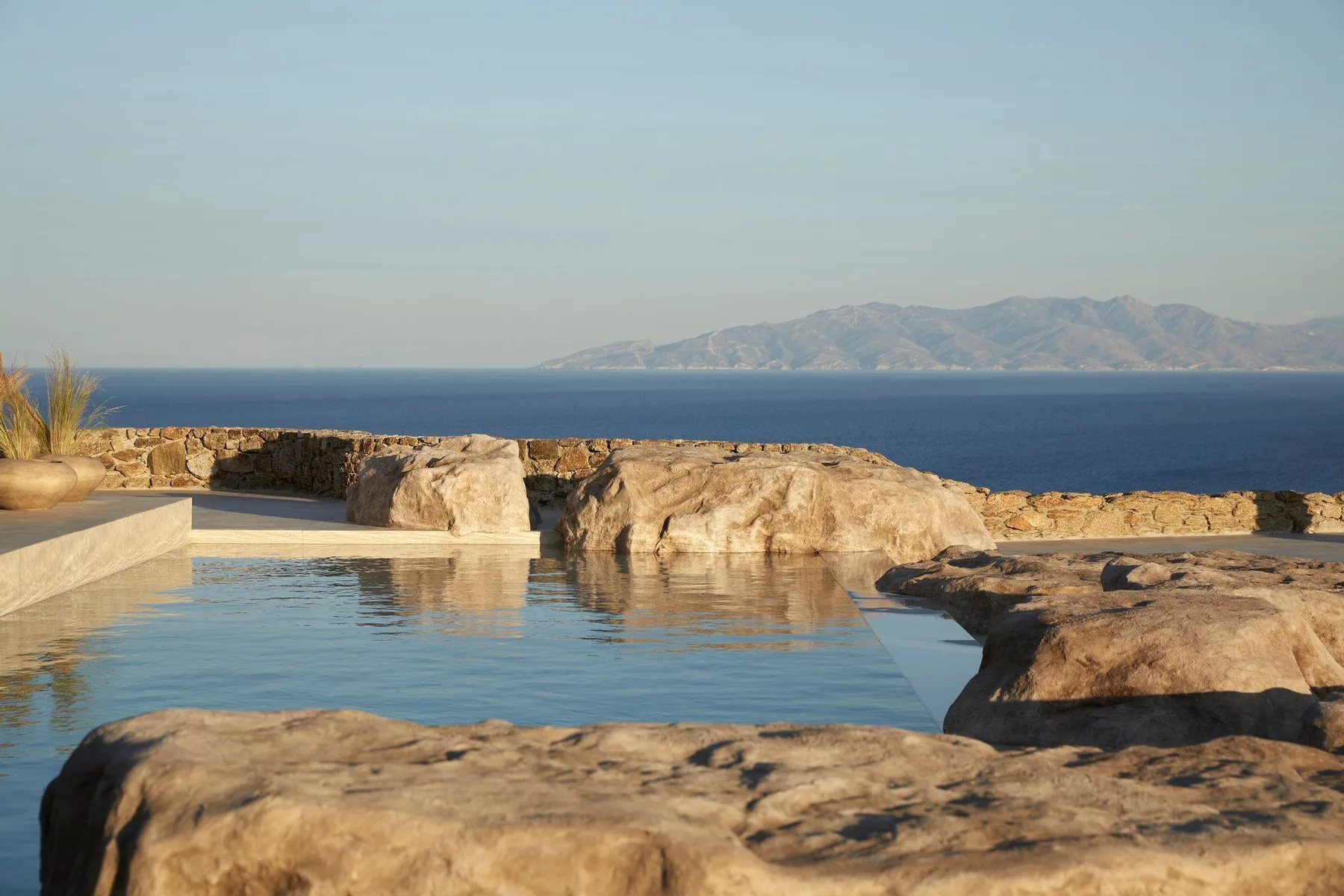 An outdoor pool beside rocky terrain overlooks the sea and distant mountains.