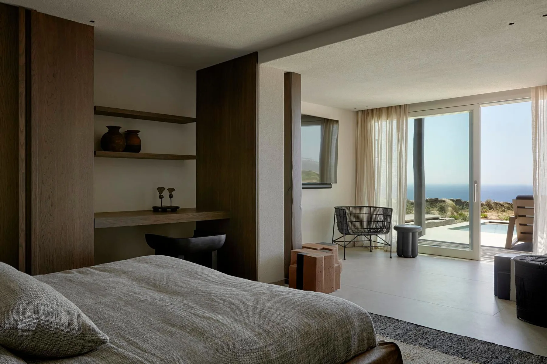 A bedroom opens onto a bright sitting area with large windows overlooking the sea.