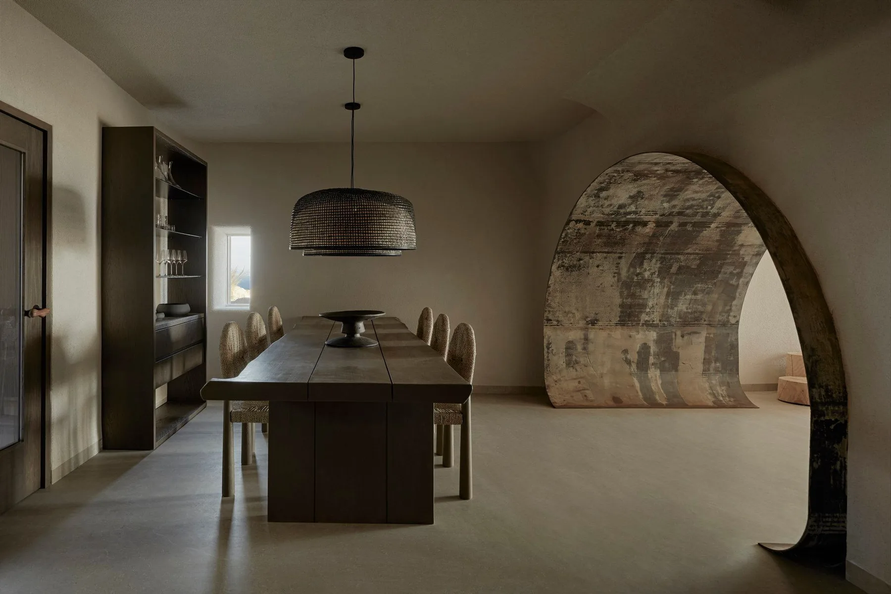 A dining room with a long table beneath a pendant light and a curved partition.