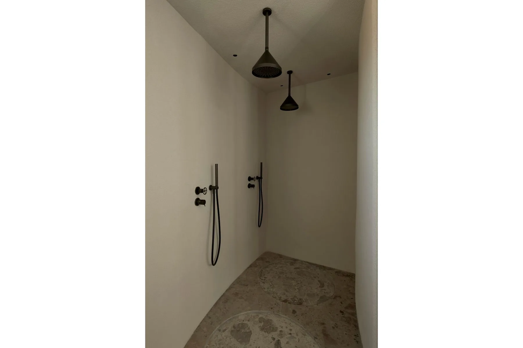 A shower area with wall-mounted fixtures and a stone-patterned floor.