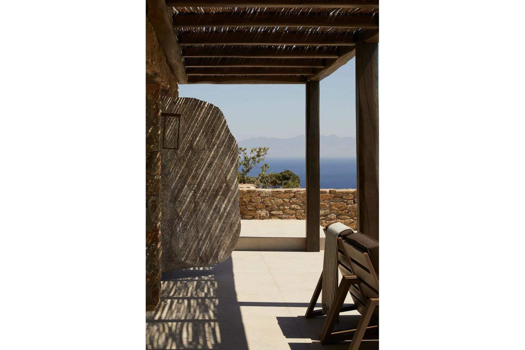 A shaded outdoor terrace overlooks the sea, with seating beside a low stone wall.