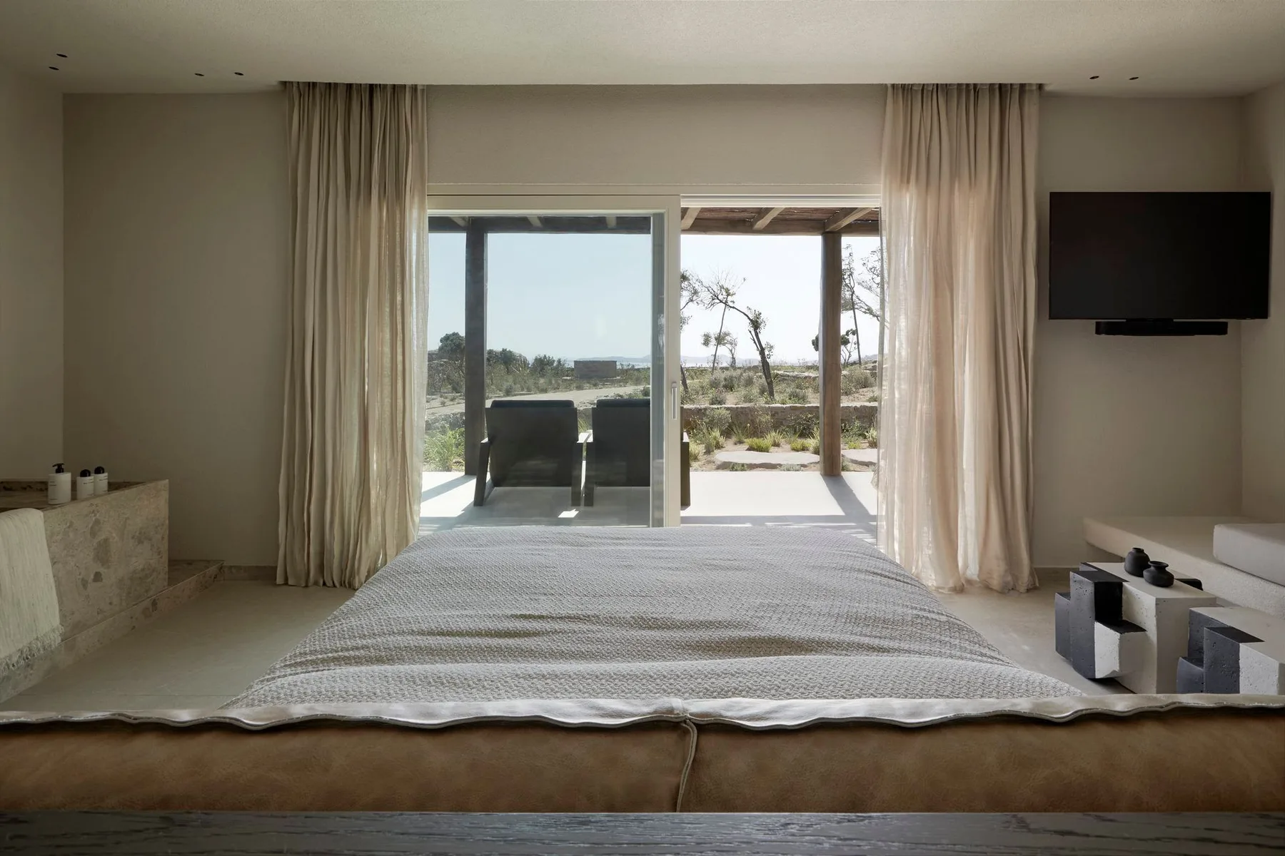 A bedroom with a neatly made bed facing glass doors and a patio.