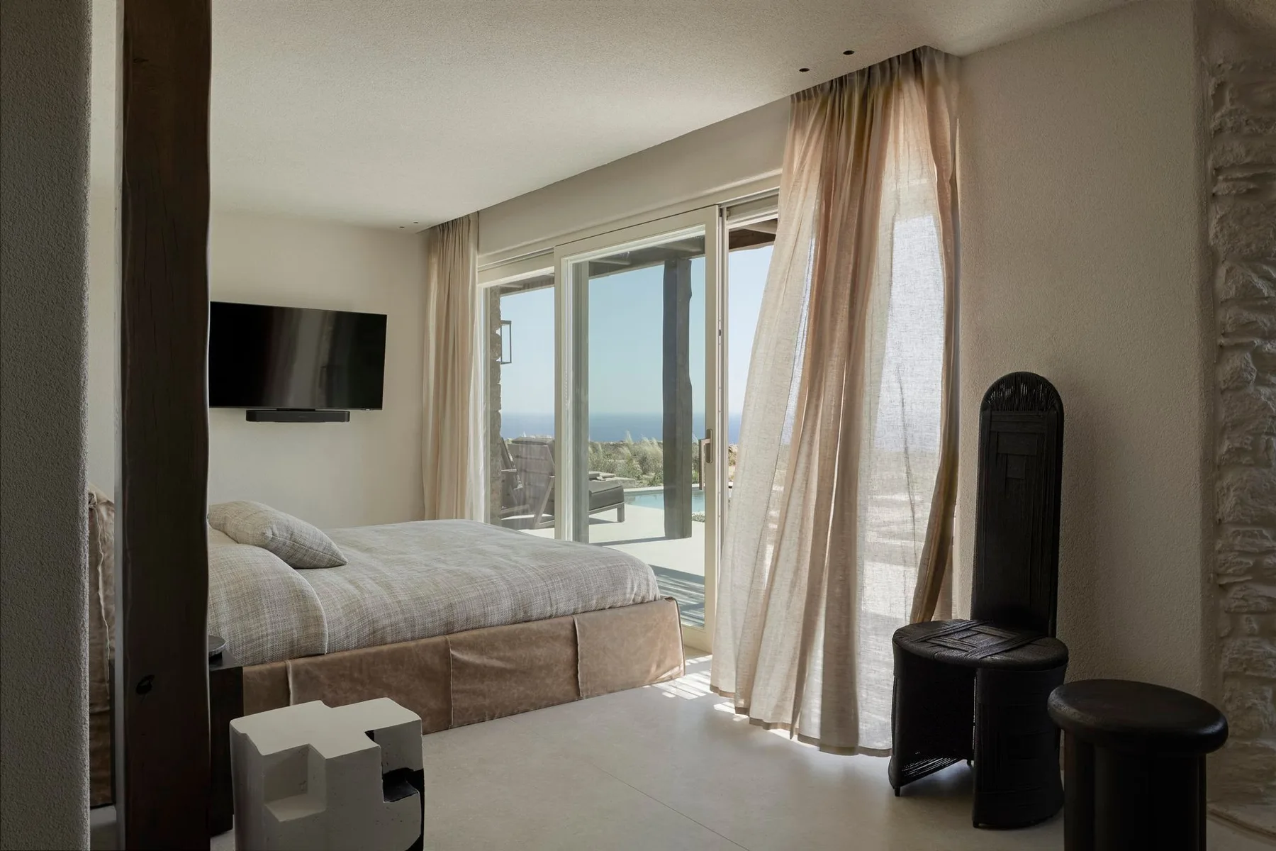 A bedroom with a bed beside glass doors opening onto a sea view.