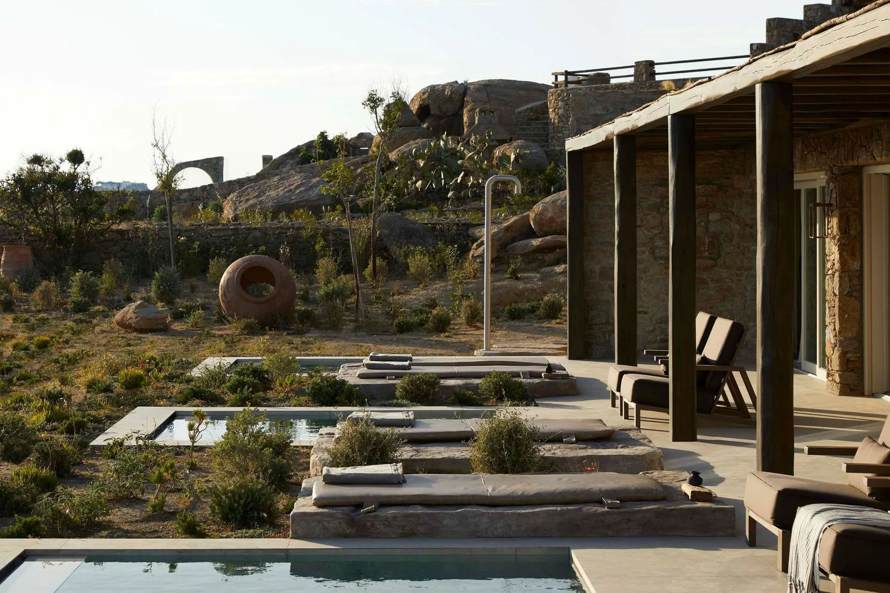 A rocky desert landscape surrounds a patio with tiered pools and outdoor seating.