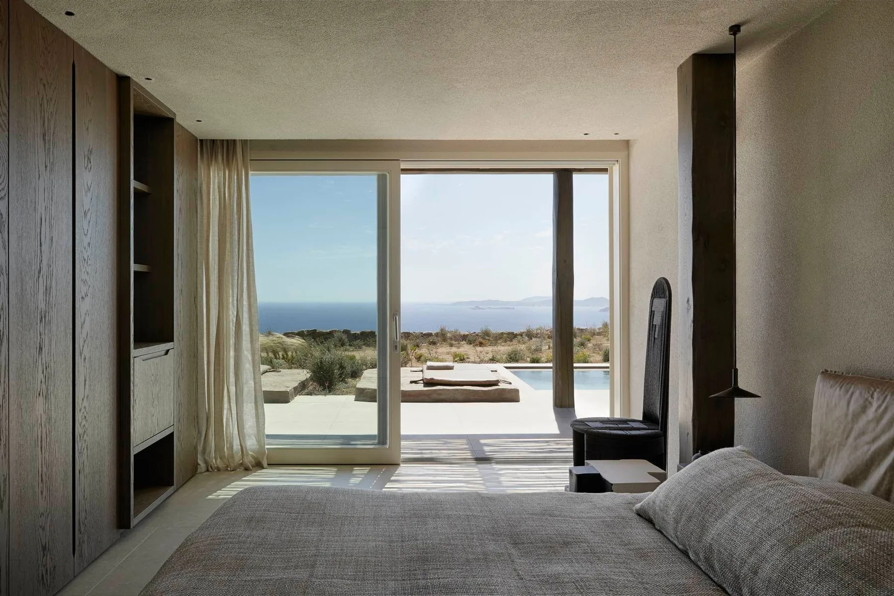 A bedroom opens through sliding glass doors to a terrace with a pool and ocean view.