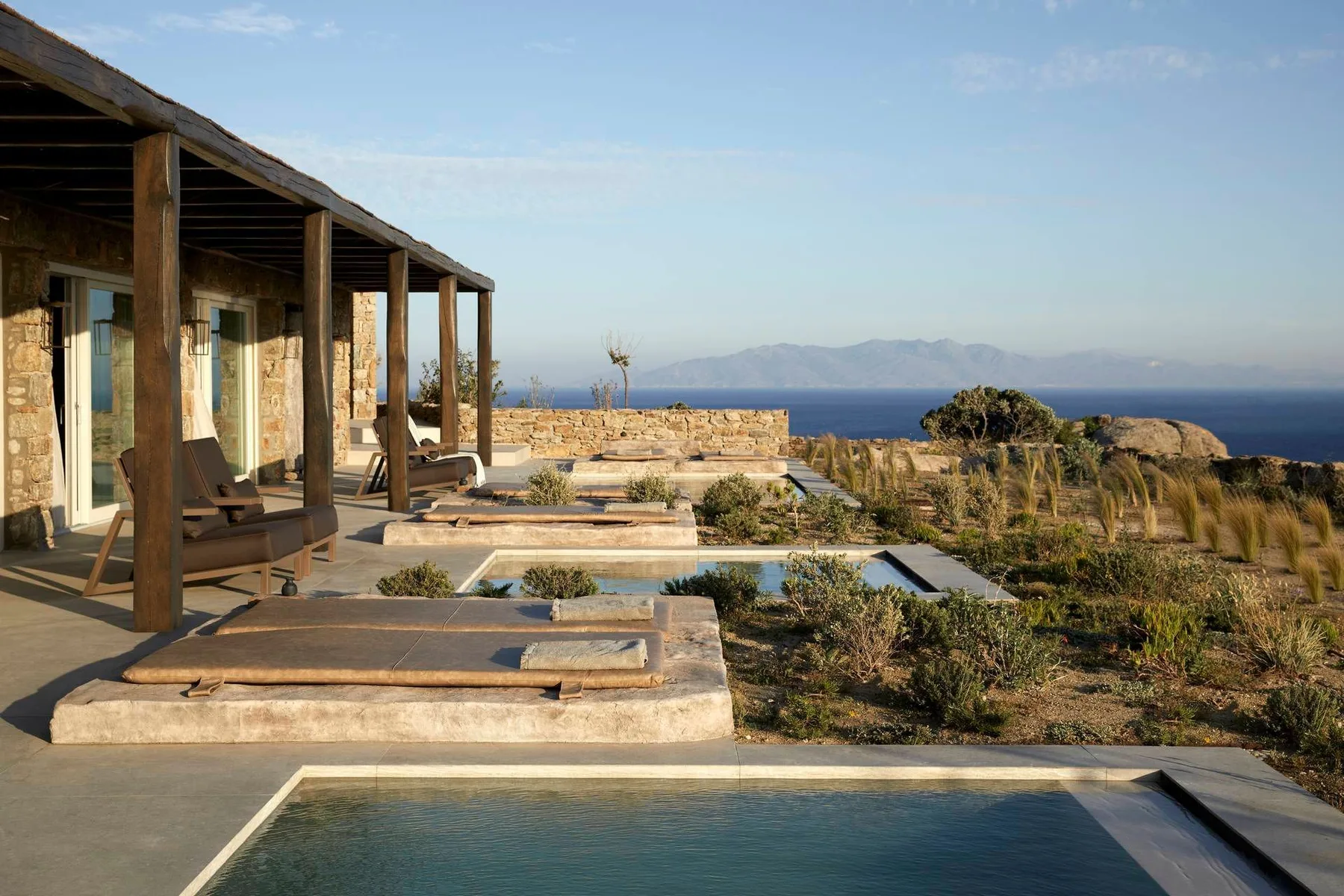 A covered patio with seating overlooks a pool and distant water.
