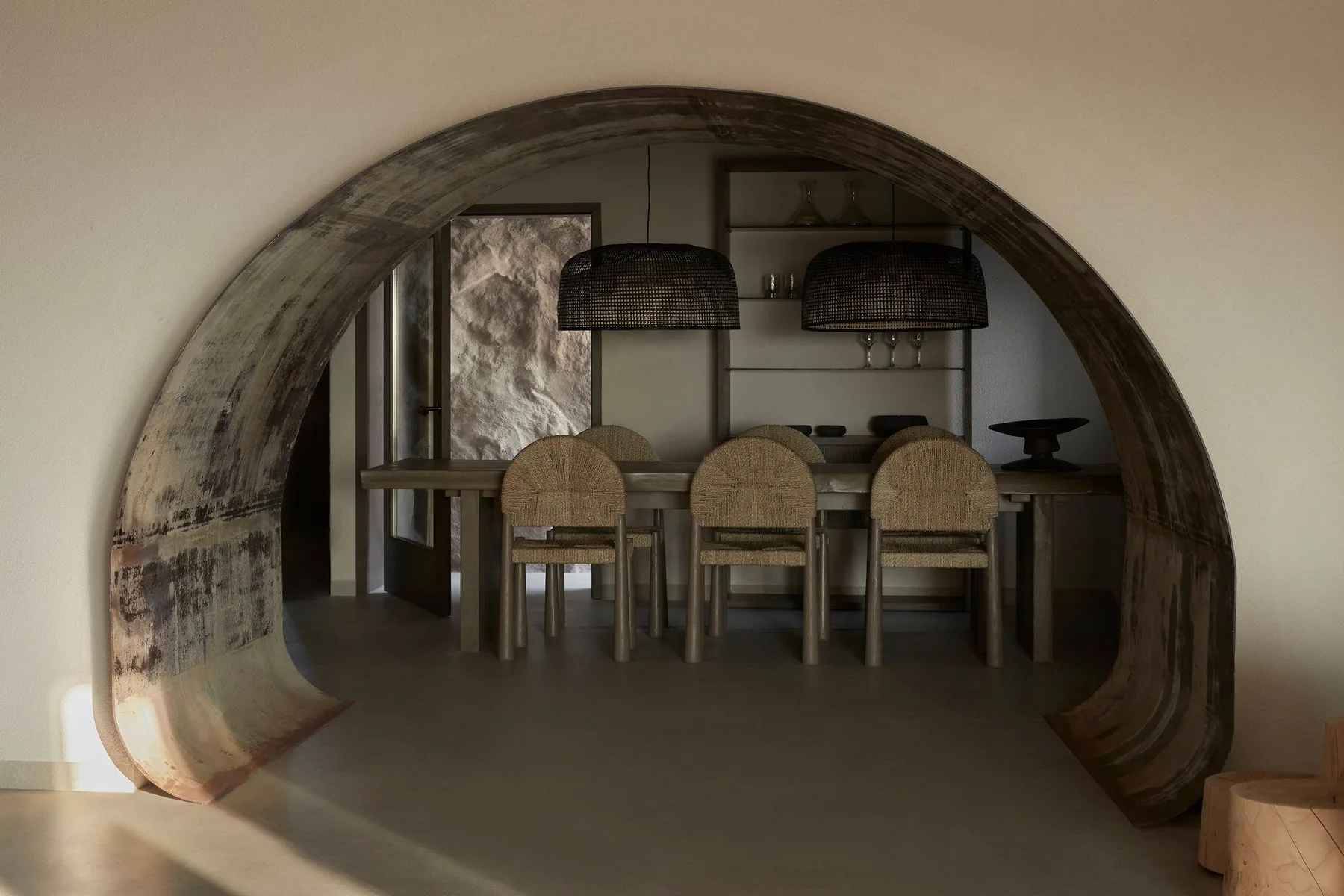 A dining area is framed by a large curved opening, with a table and seating.