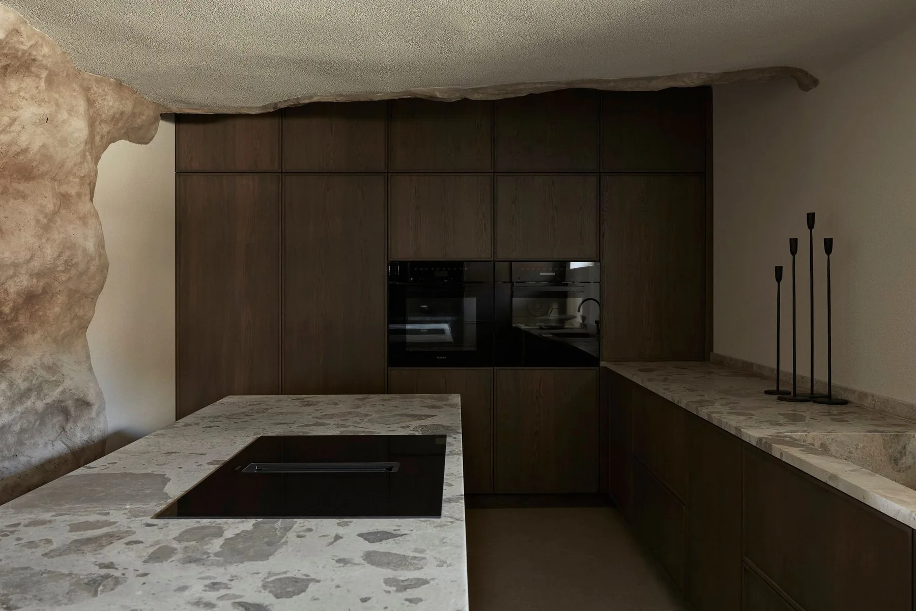 A modern kitchen with dark cabinetry, built-in appliances, and stone countertops.