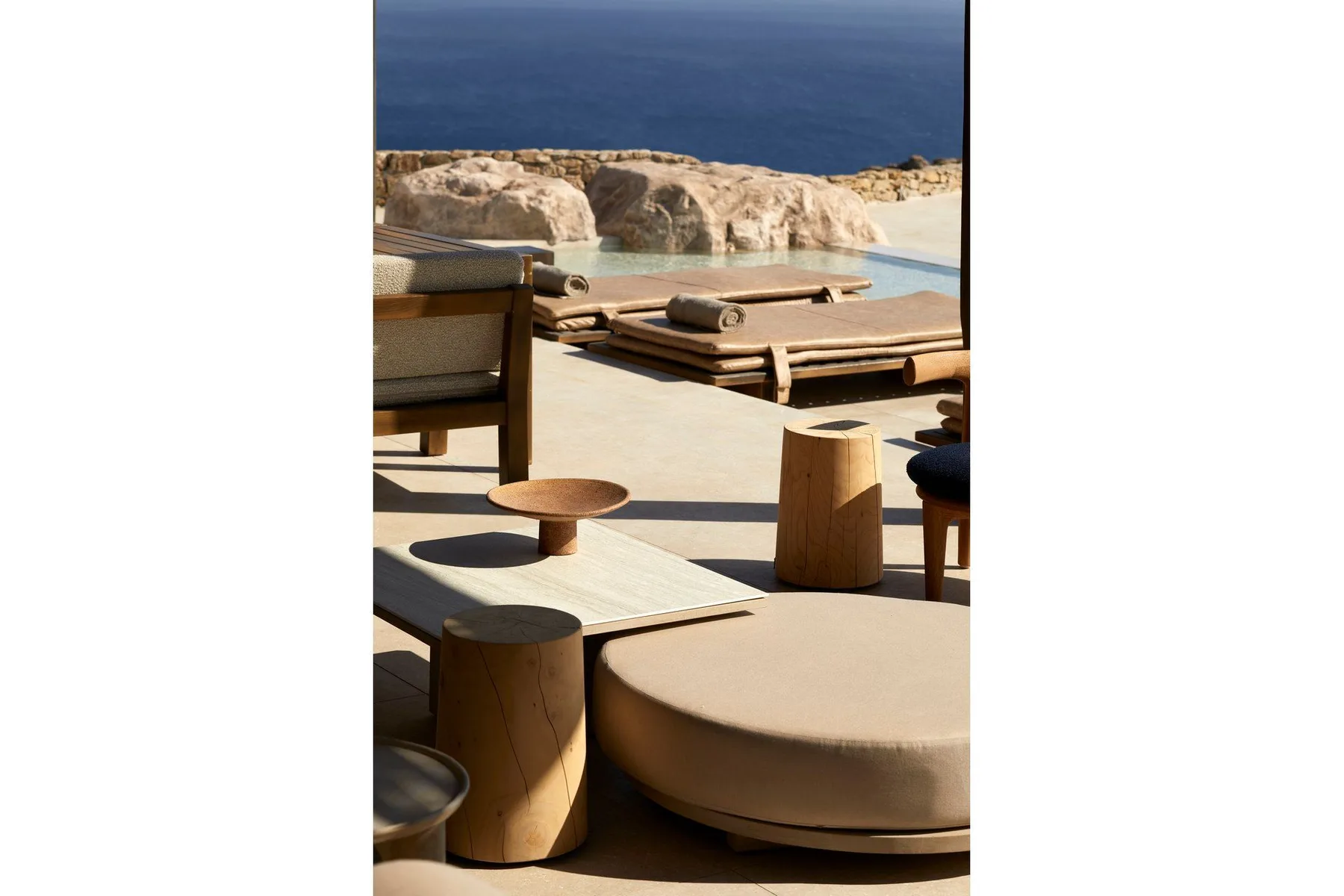 An outdoor terrace seating area overlooks the sea, with a pool beyond the loungers.